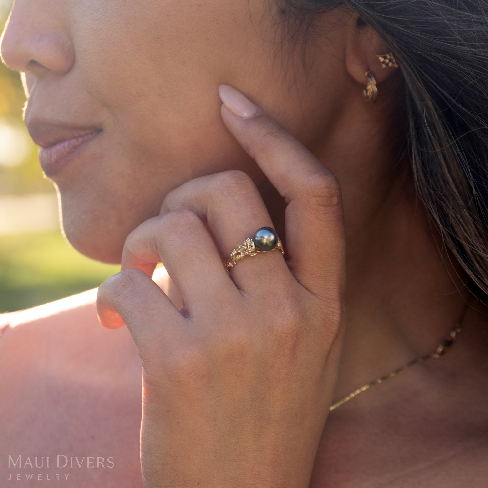 Close-up of a woman wearing a 14k yellow gold ring with a Tahitian black pearl, outdoors.