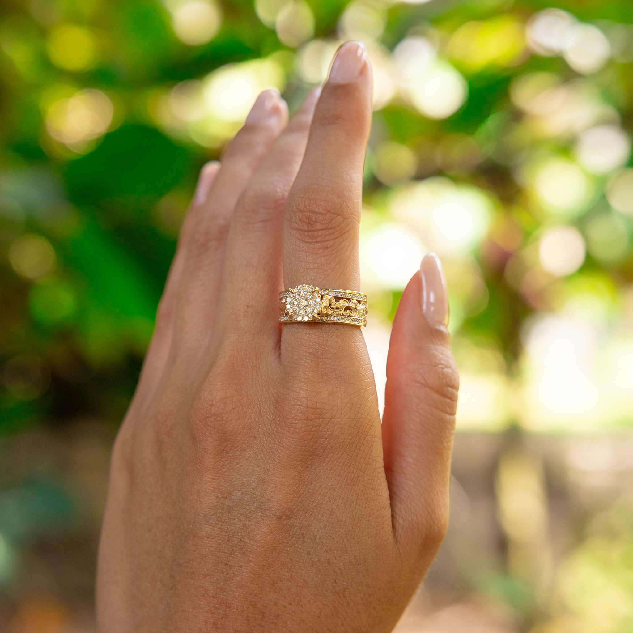 Woman's hand wearing a Living Heirloom Engagement Ring in Gold with Diamonds with a blurry green background
