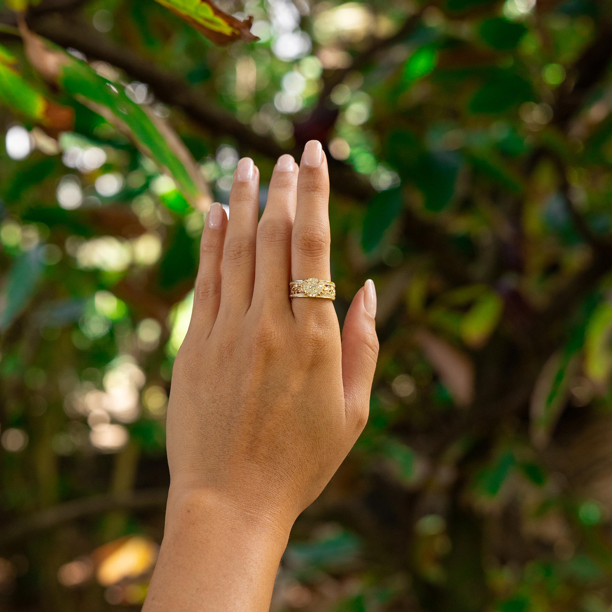 Woman's hand held up in a garden wearing a Living Heirloom Engagement Ring in Gold with Diamonds