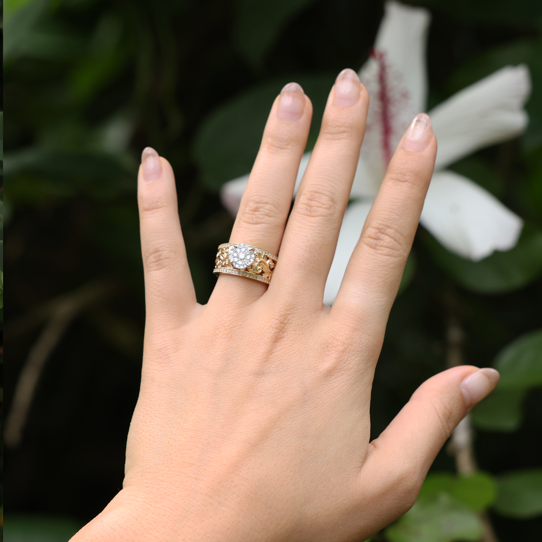 A woman's hand with a Living Heirloom Engagement Ring in Gold with Diamonds with flower and leaves in the back
