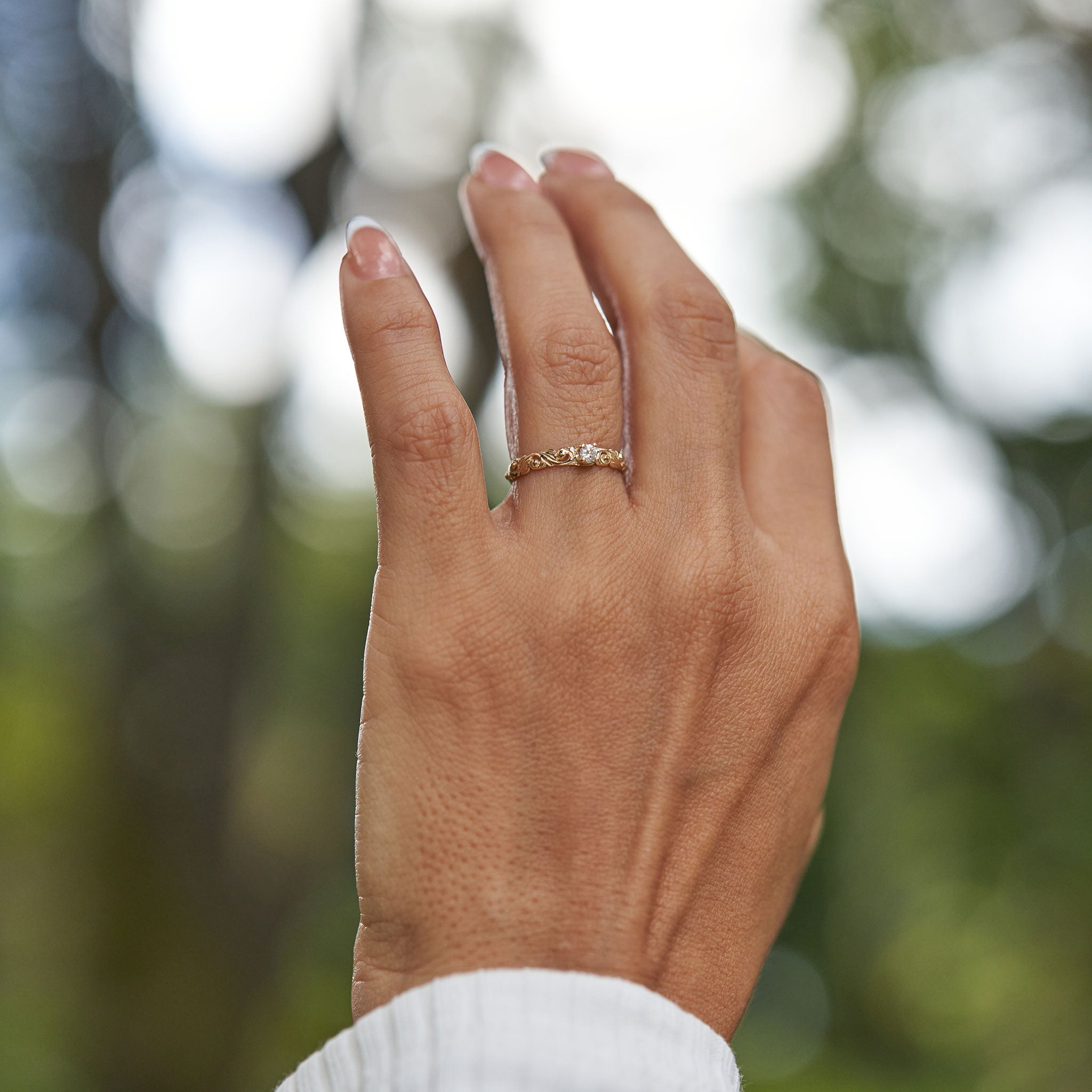 Hand wearing a Living Heirloom Ring in 14k Yellow Gold with Diamond and blurry green background
