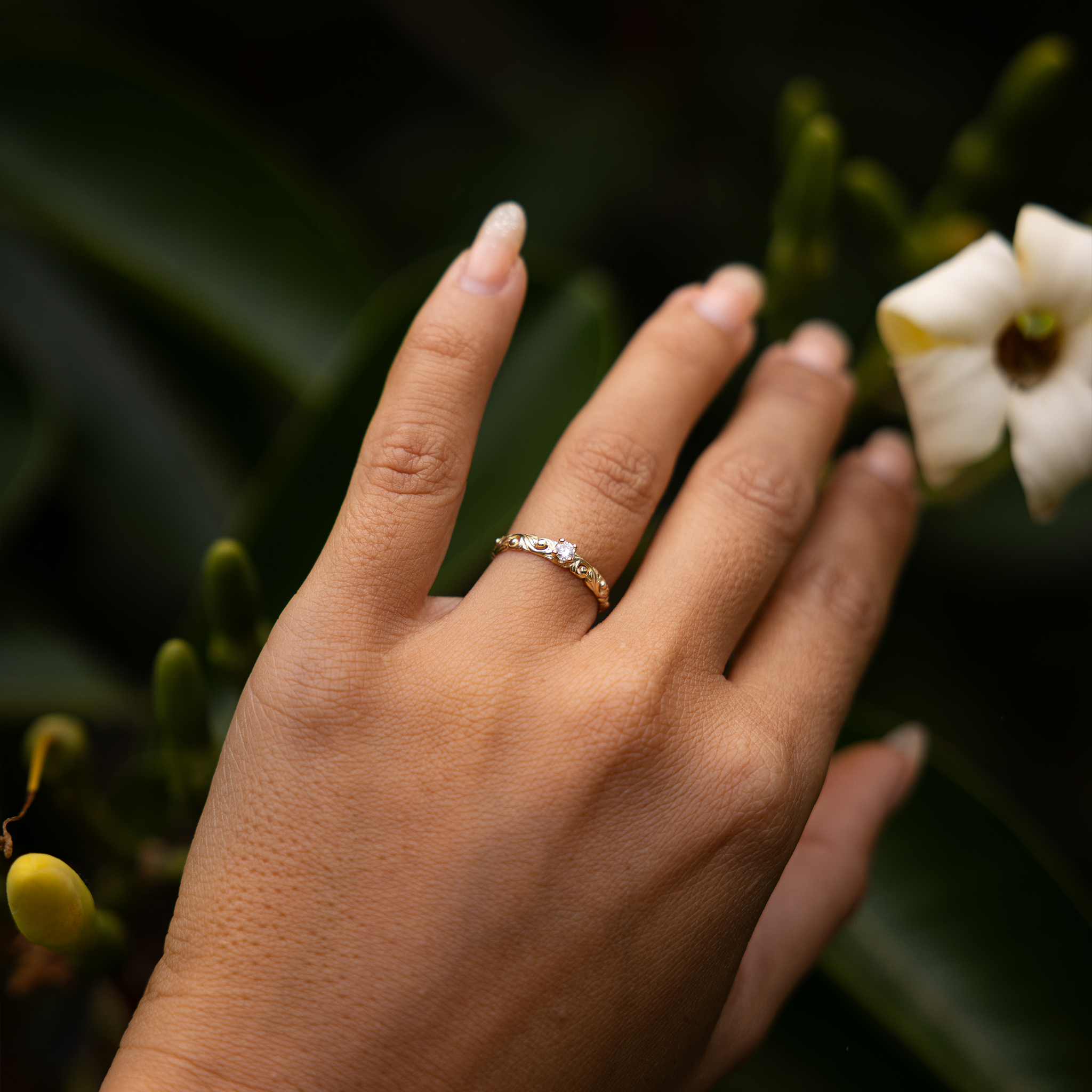 Hand wearing a Living Heirloom Ring in 14k Yellow Gold with Diamond with a leaf and flower background