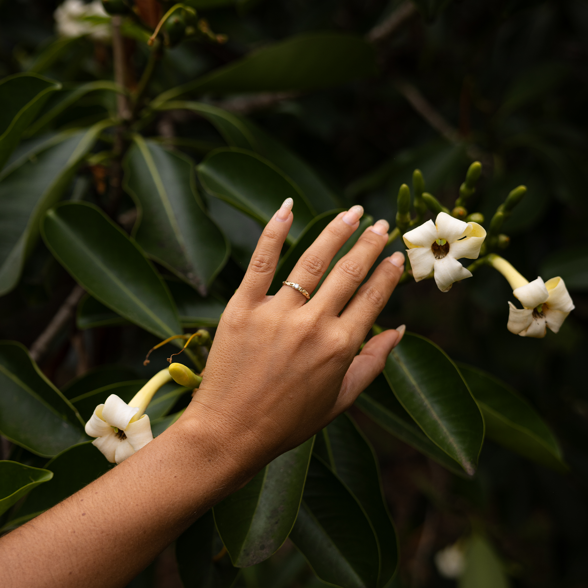 Hand wearing a Living Heirloom Ring in 14k Yellow Gold with Diamond with a leaf and flower background