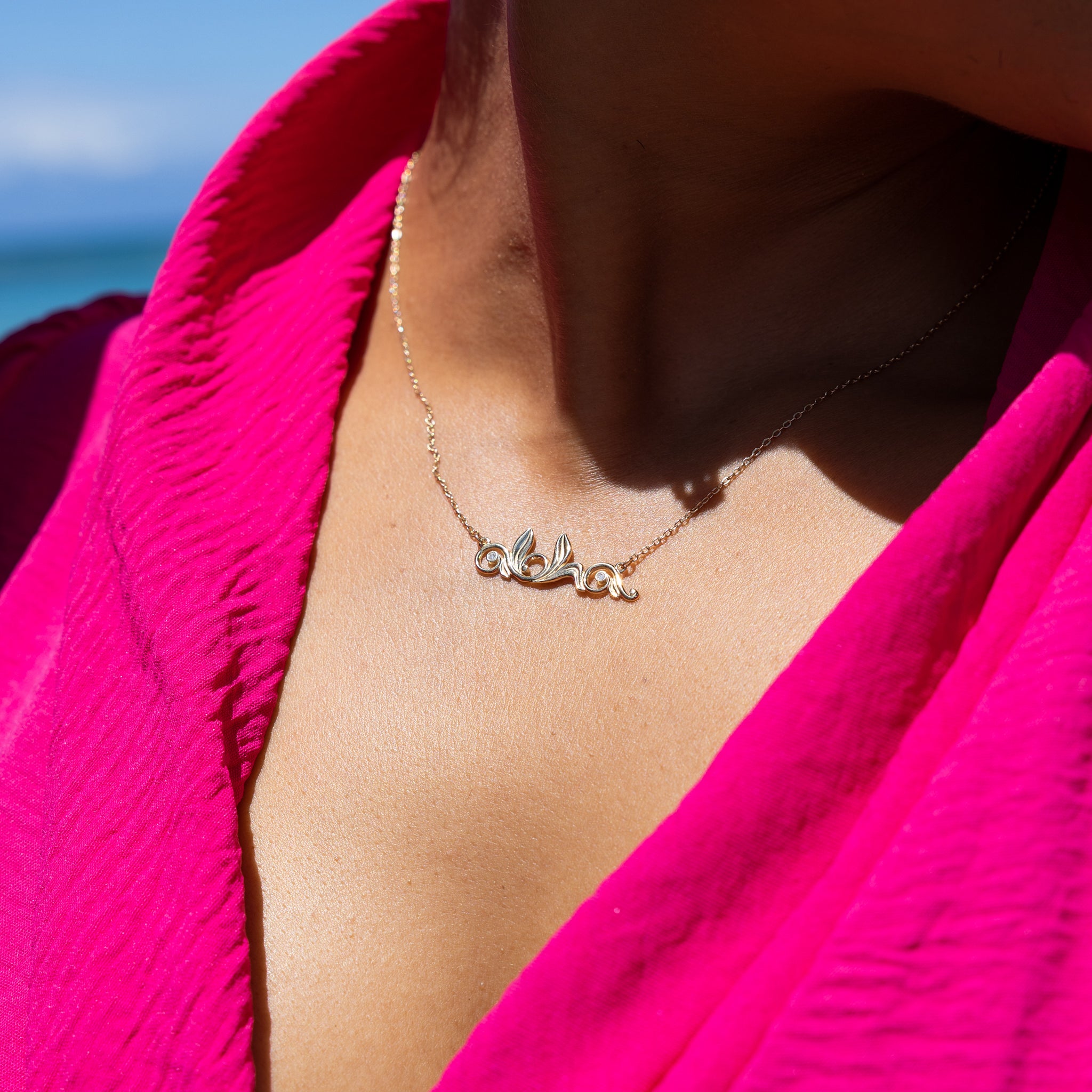 Woman's chest wearing a pink top and a Living Heirloom Aloha Necklace in Gold with Diamonds outdoors