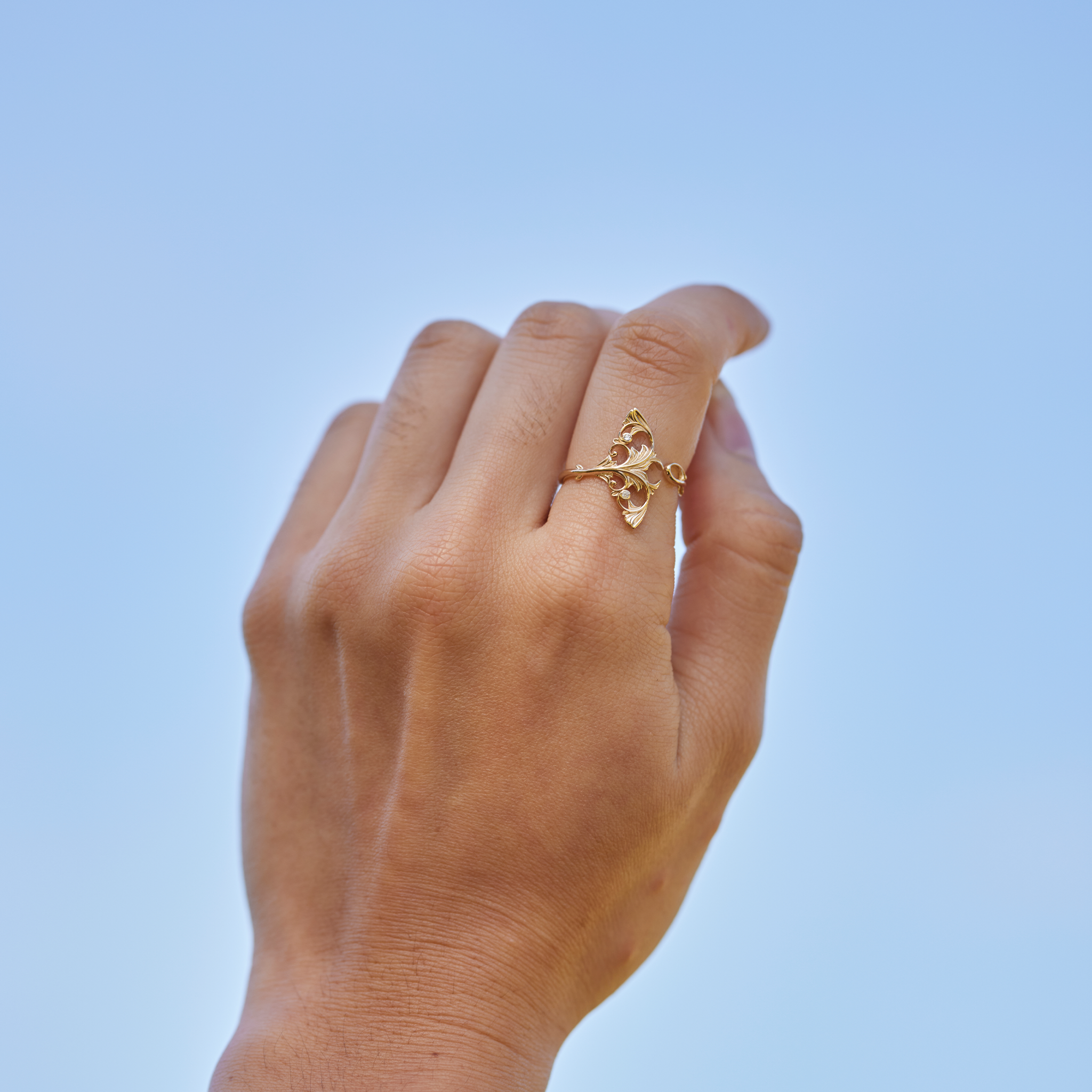 Living Heirloom Manta Ray Ring in Gold with Diamonds on a hand held up against a blue sky