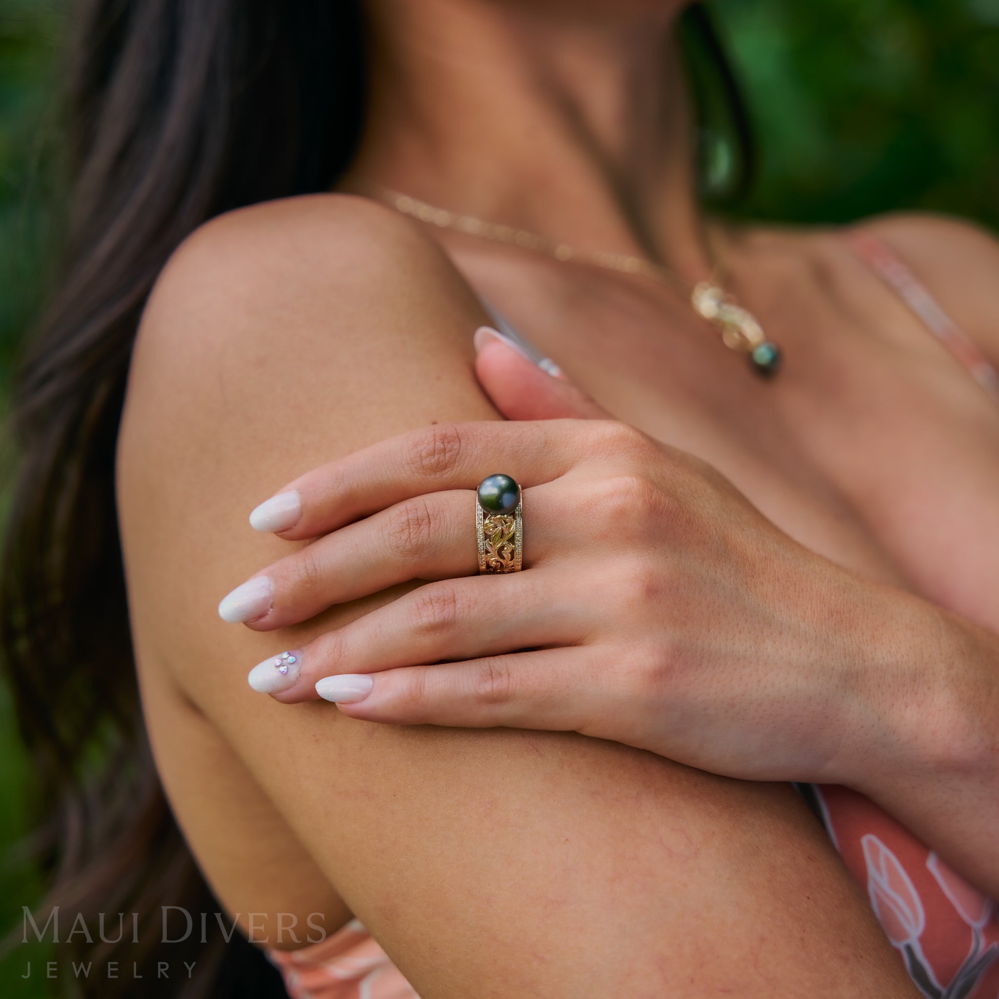 Close-up of a hand wearing a Living Heirloom Tahitian Black Pearl Ring in Gold with Diamonds with blurred background
