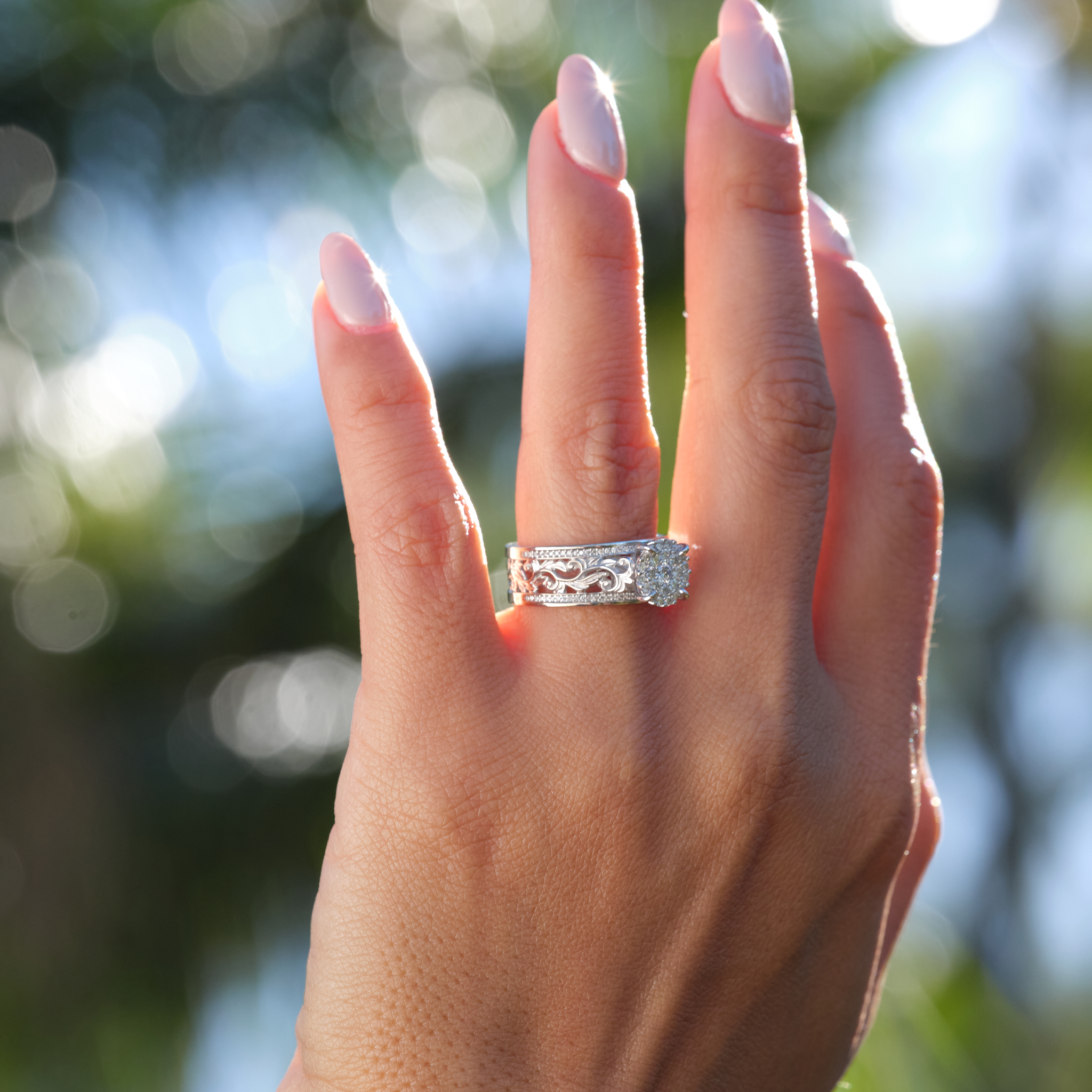 Woman's hand with a Hawaiian Heirloom Engagement Ring in White Gold with Diamonds and blurred trees in background