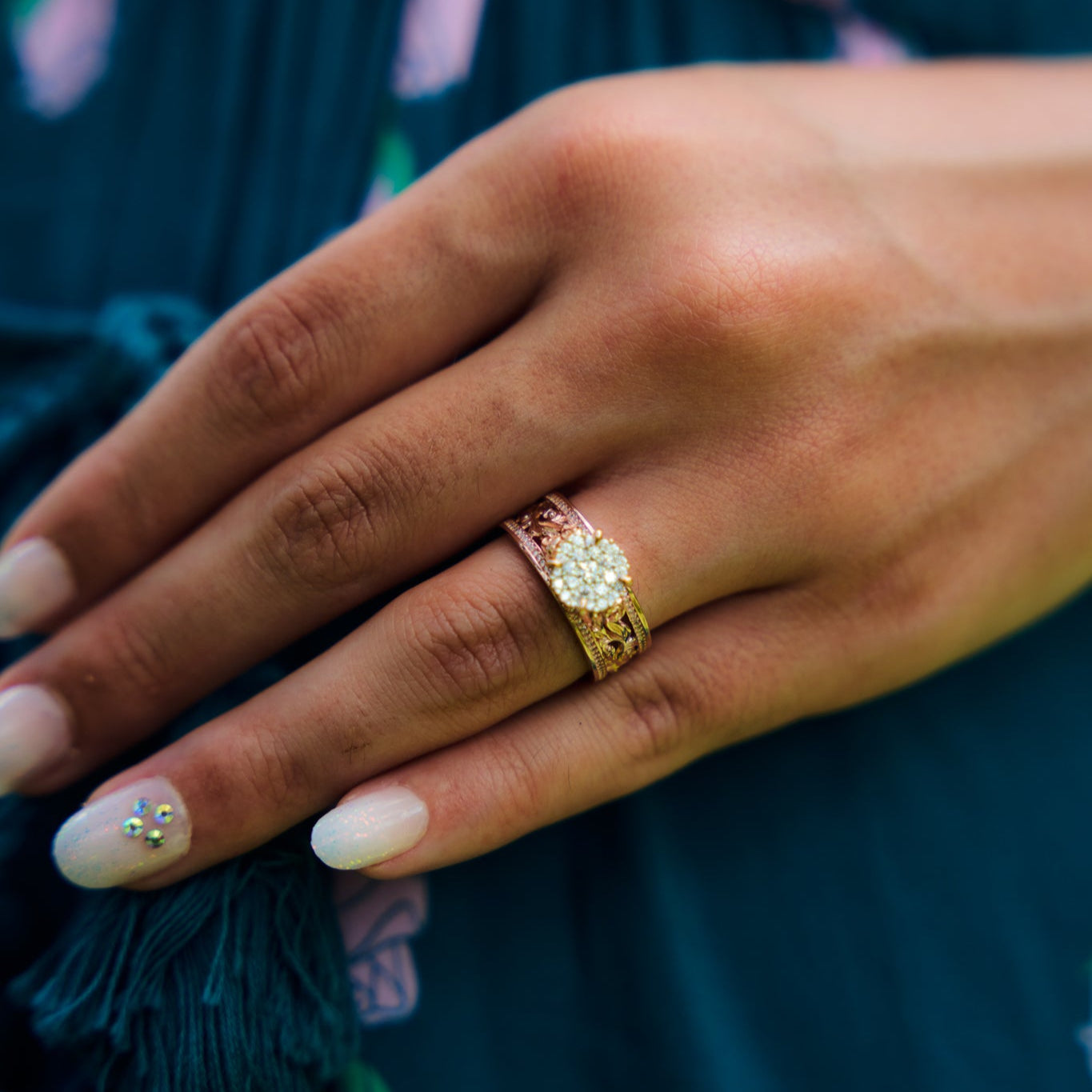 Close-up of a hand wearing a Living Heirloom Engagement Ring in Rose Gold with Diamonds against a blurred dress