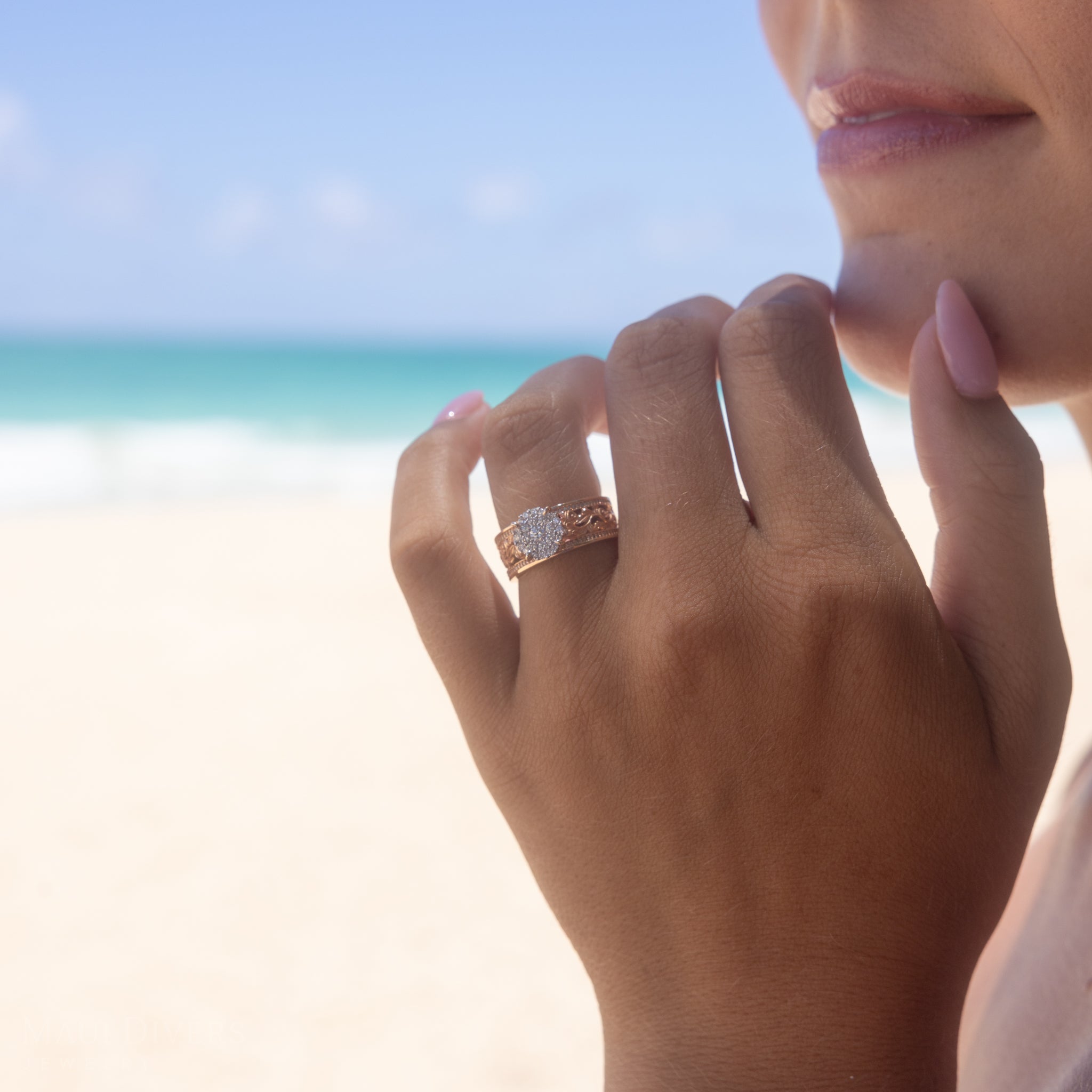 Close-up of a hand wearing a Living Heirloom Engagement Ring in Rose Gold with Diamonds with a beach background