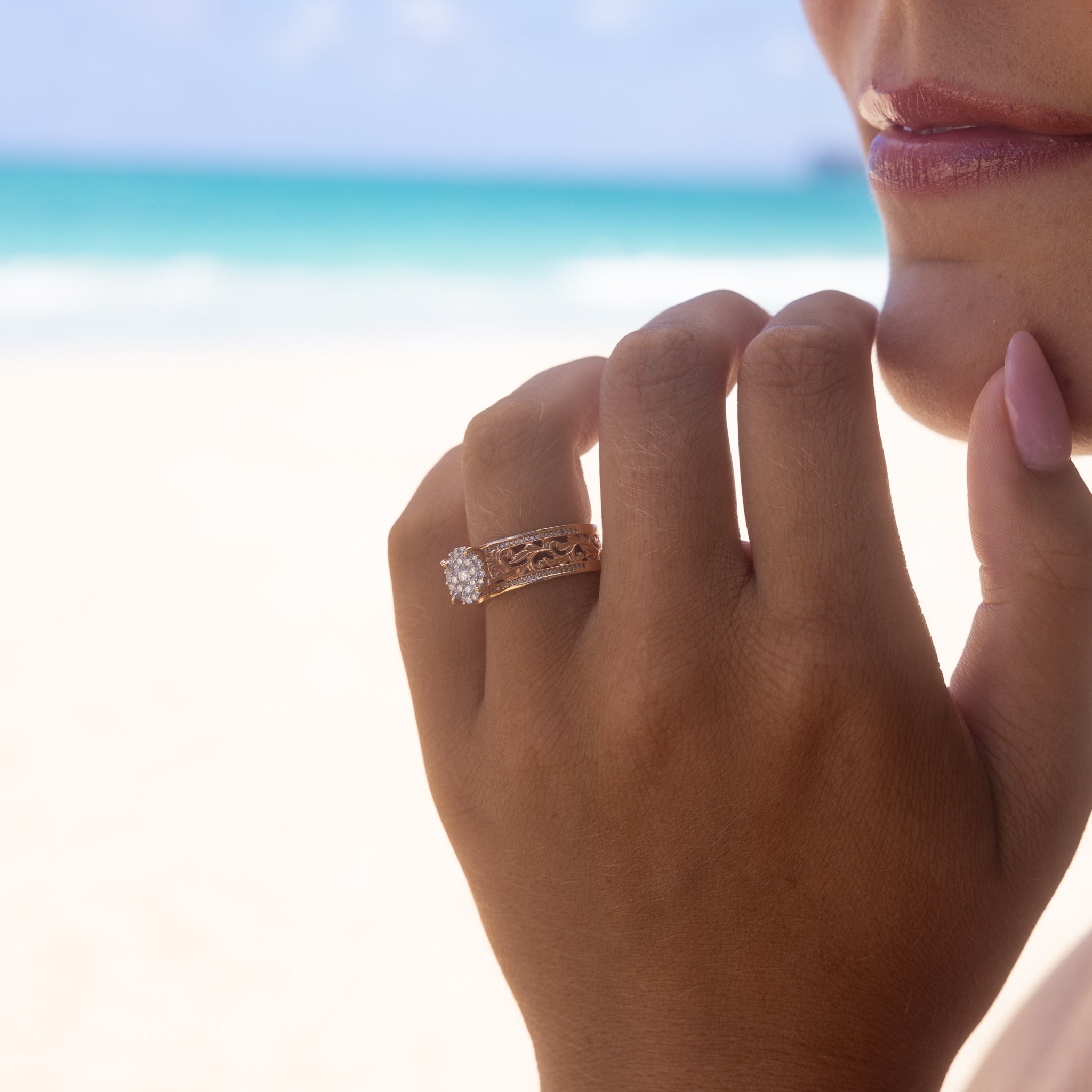 Close-up of a hand wearing a Living Heirloom Engagement Ring in Rose Gold with Diamonds with a beach background