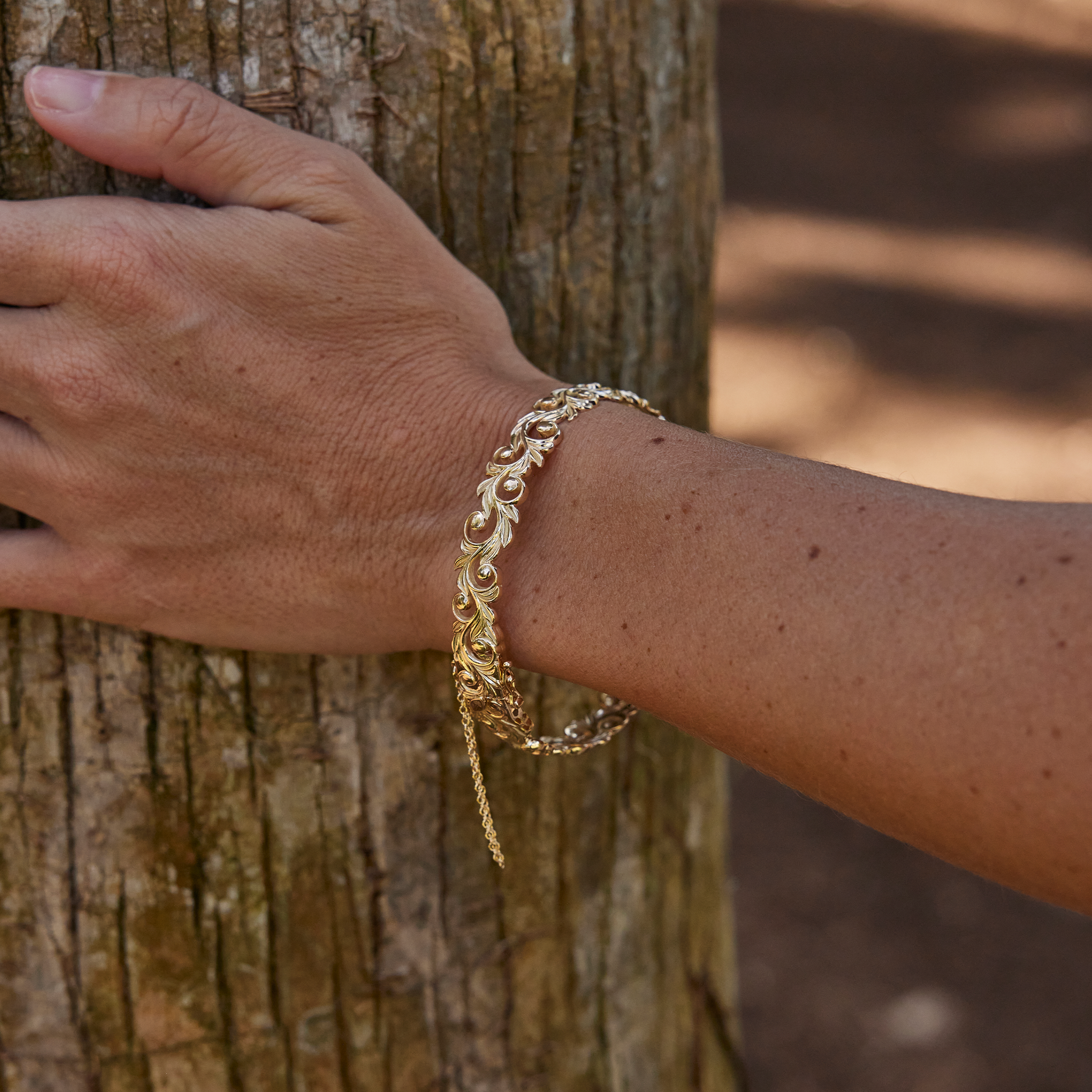Living Heirloom Hinge Bracelet in 14k Yellow Gold on a wrist holding a tree trunk