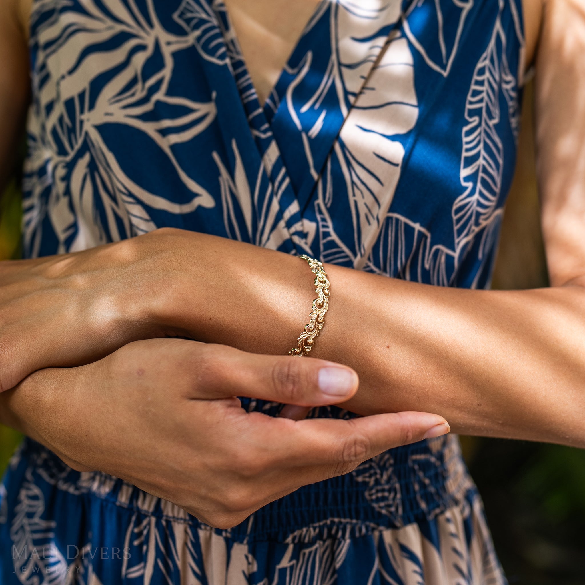 Close-up of a Living Heirloom Hinge Bracelet in 14k Yellow Gold on a wrist with a blurred blue dress in the back