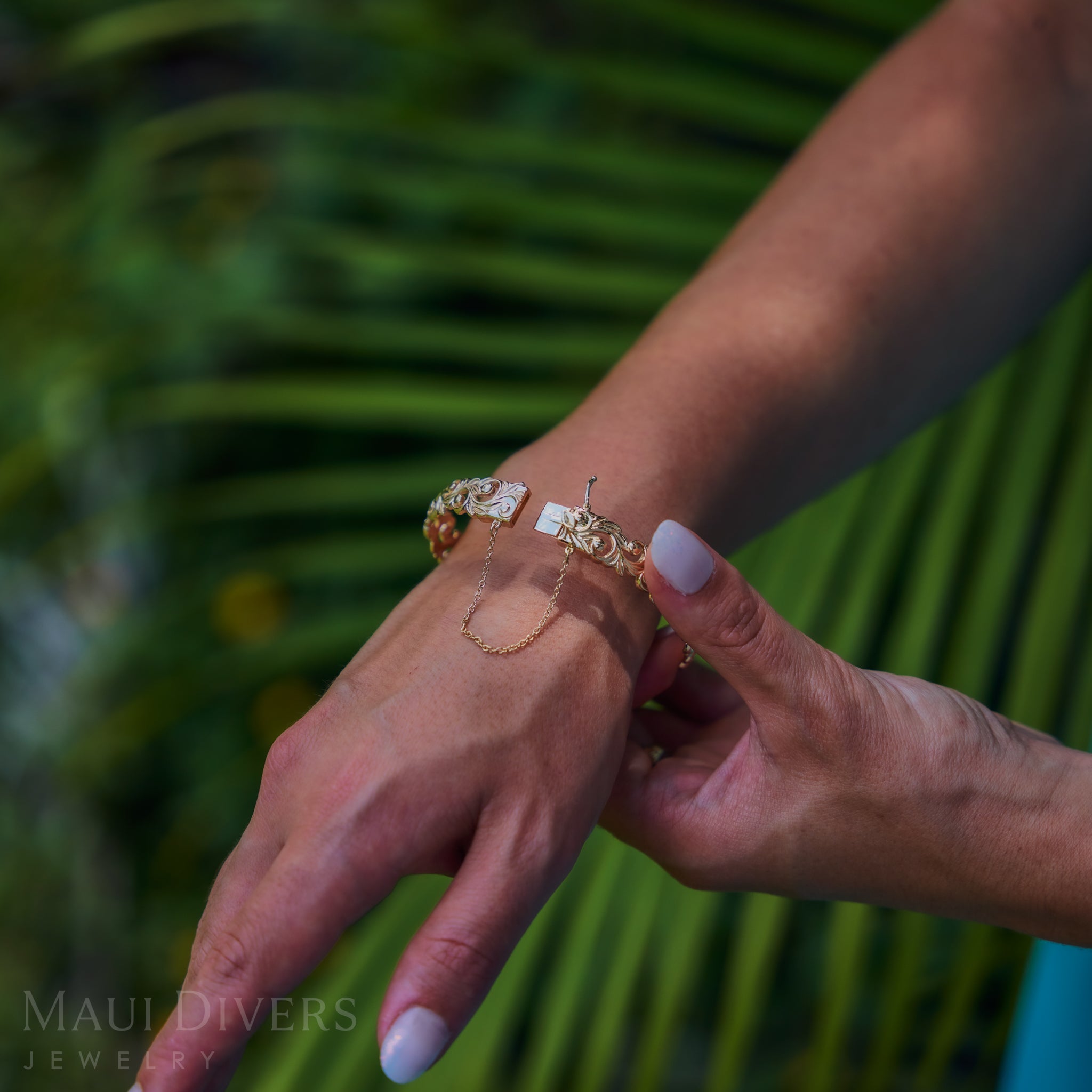 Close-up of a hand wearing a Living Heirloom Hinge Bracelet in 14k Yellow Gold with a blurred green leafy background