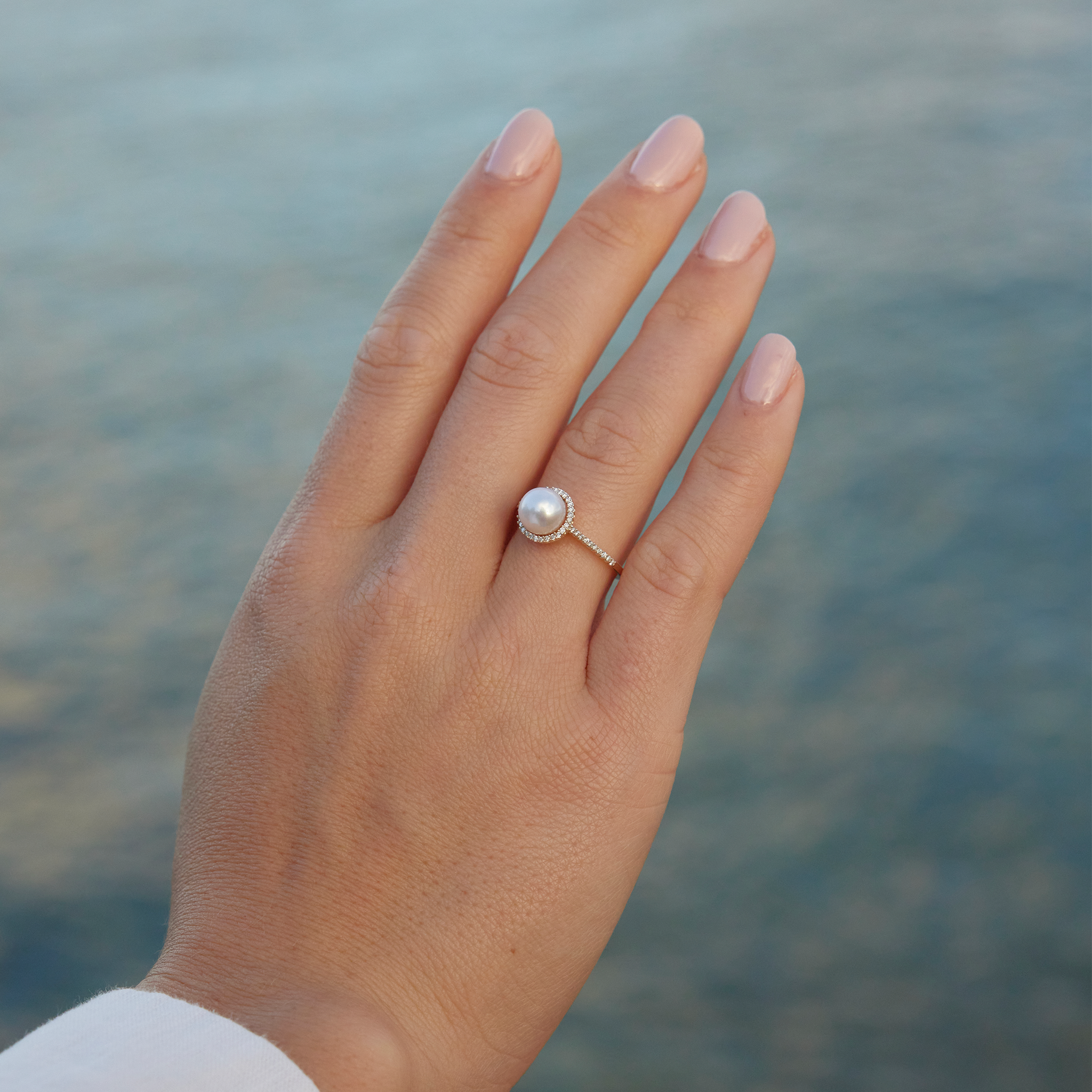 Hand over water wearing a Pick A Pearl Halo Ring in Gold with Diamonds and White Pearl