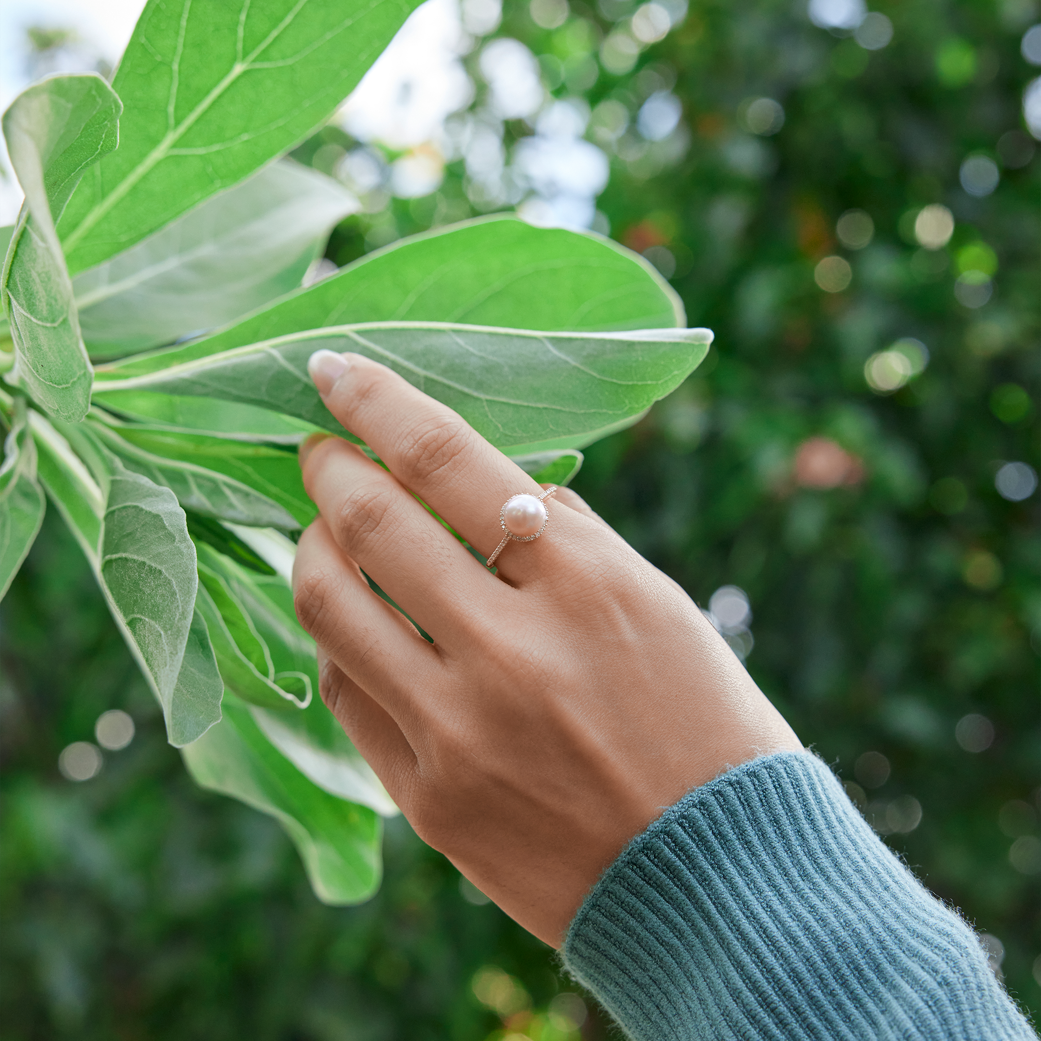 Hand holding a leaf with a Pick A Pearl Halo Ring in Gold with Diamonds and pink Pearl