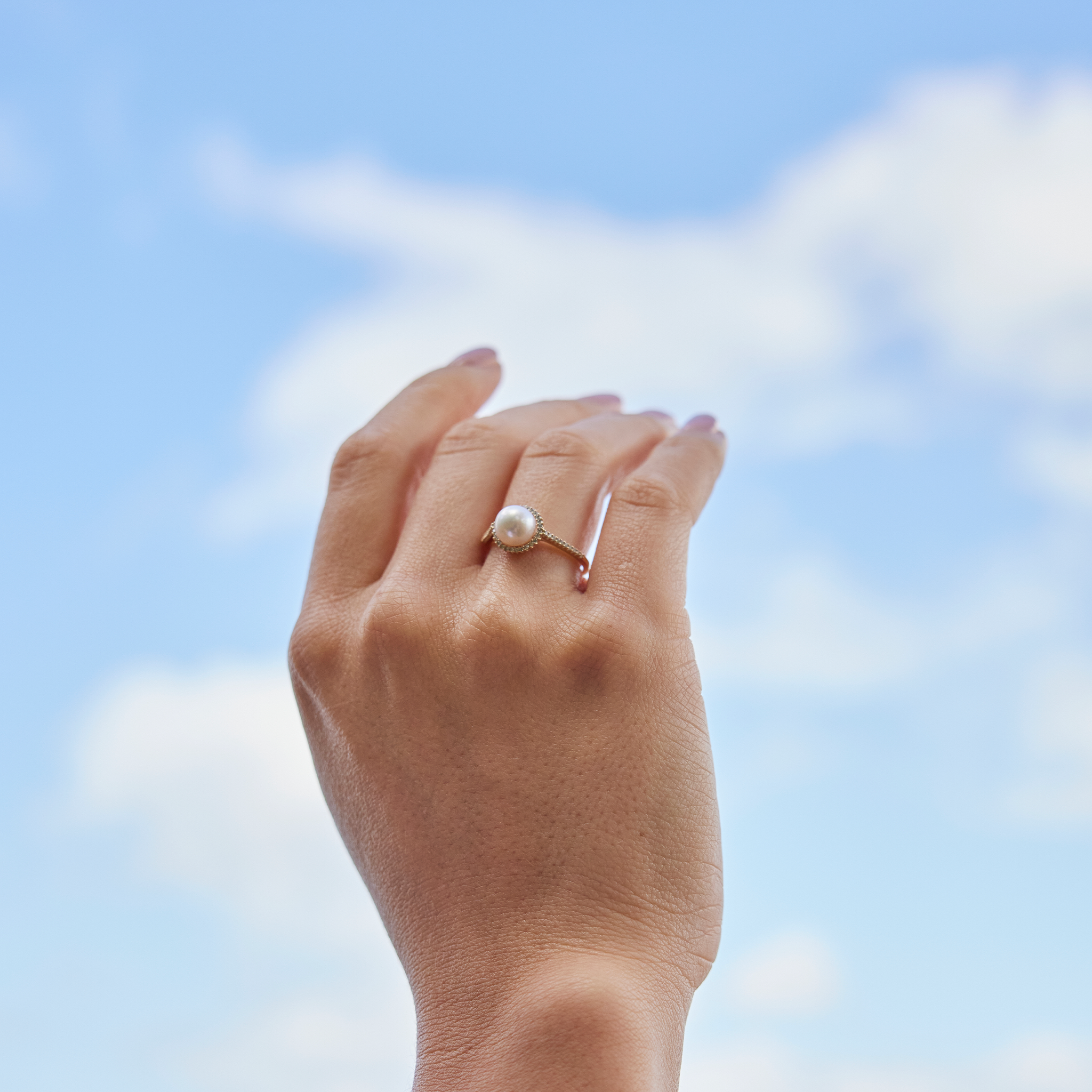 Hand against a blue sky with a Pick A Pearl Halo Ring in Gold with Diamonds and White Pearl