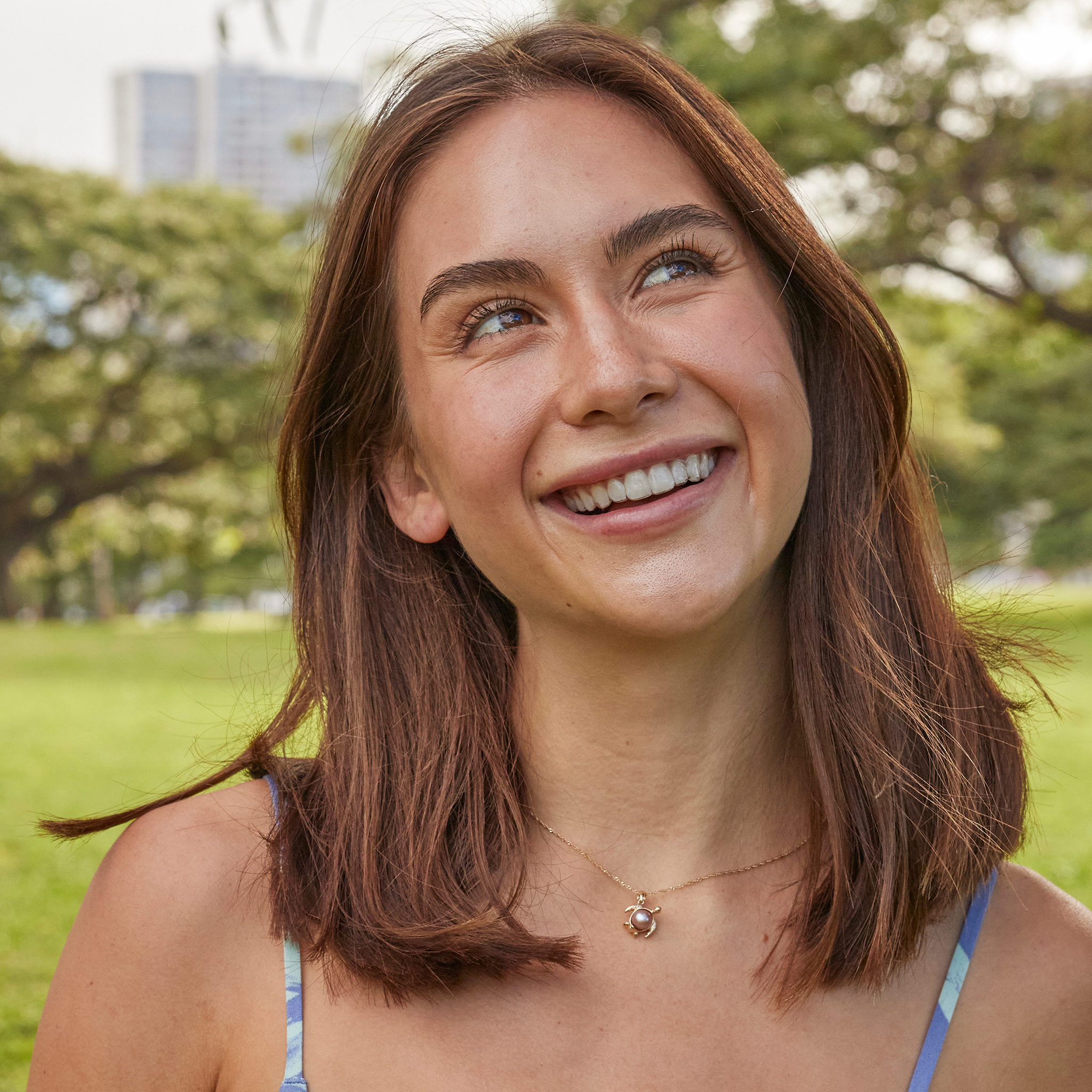 Woman in a park wearing a 12mm Pick A Pearl Honu Pendant in Gold with a Lavender Pearl
