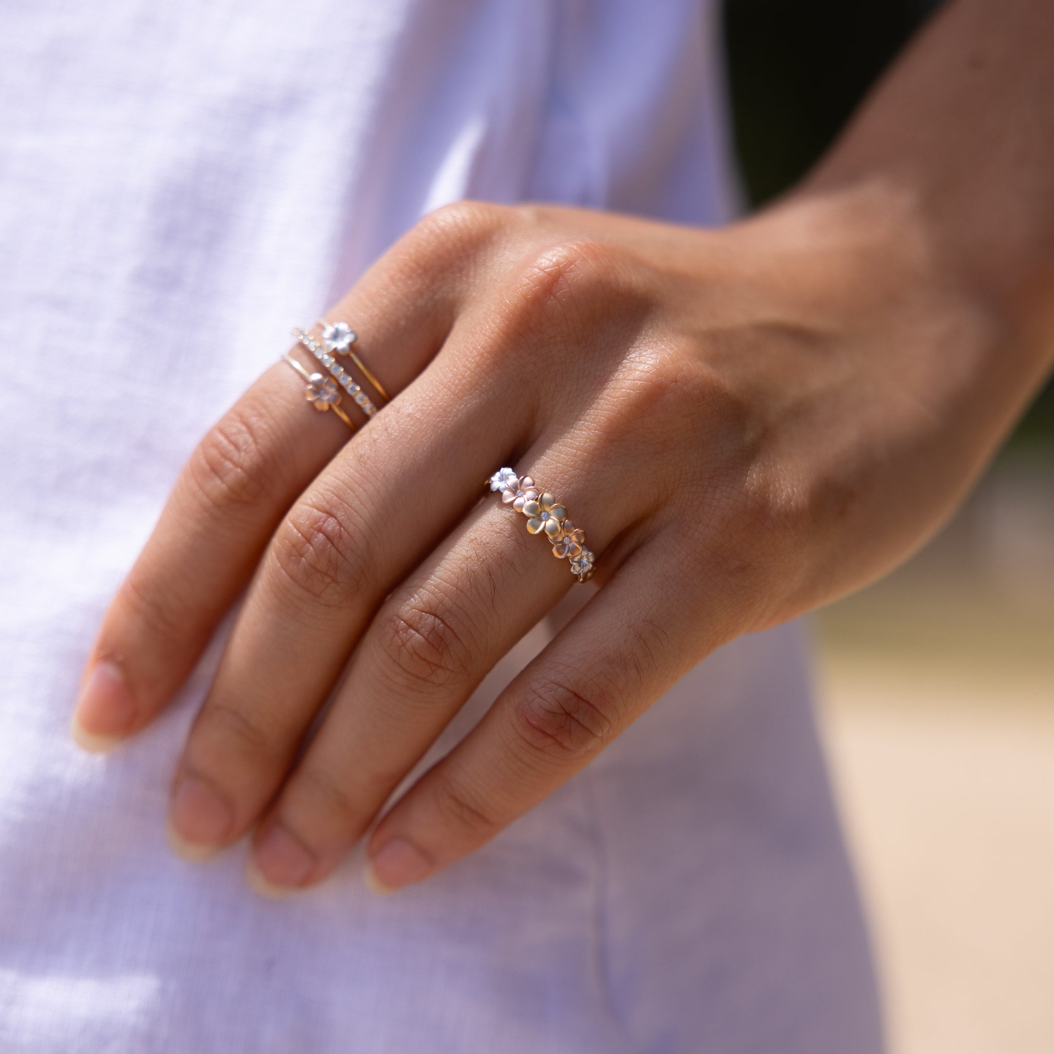 Plumeria Rings in Tri Color Gold with Diamonds on a hand against a white dress