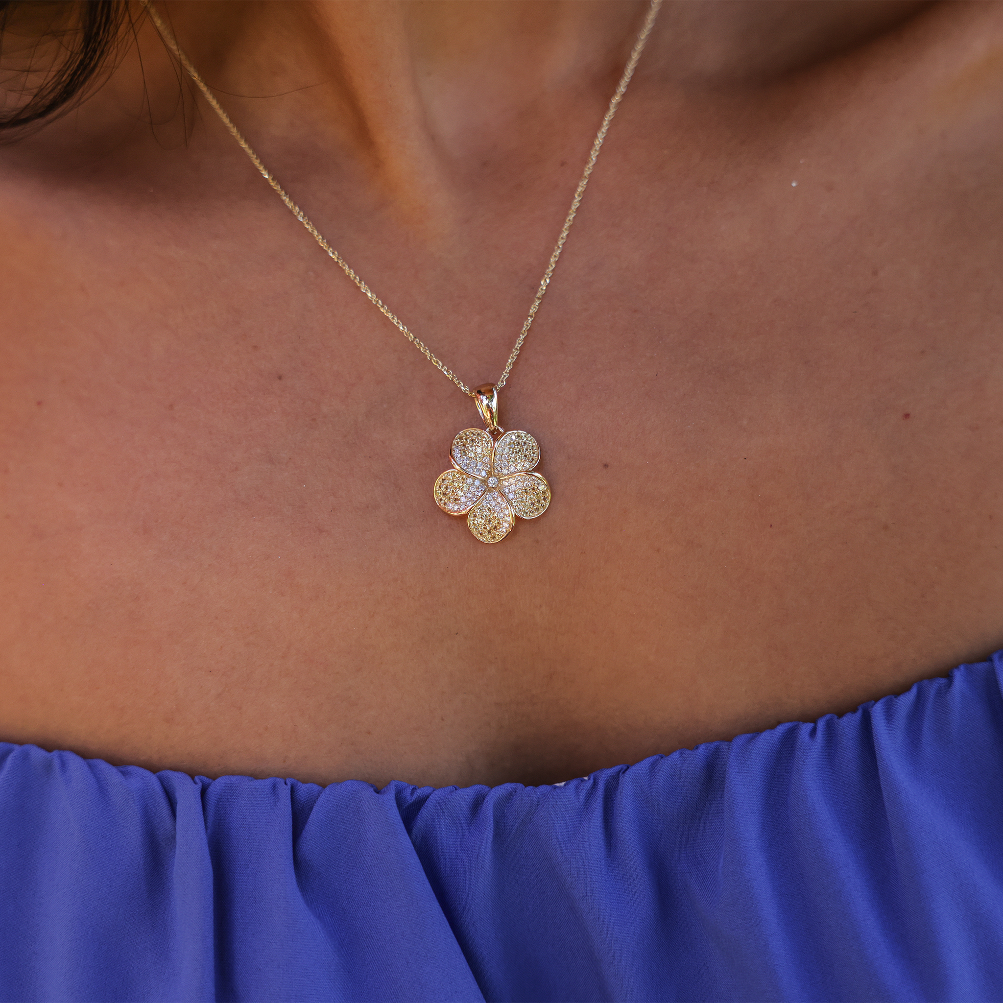 Close up of a Plumeria Yellow Sapphire Pendant in Gold with Diamonds on a person's chest