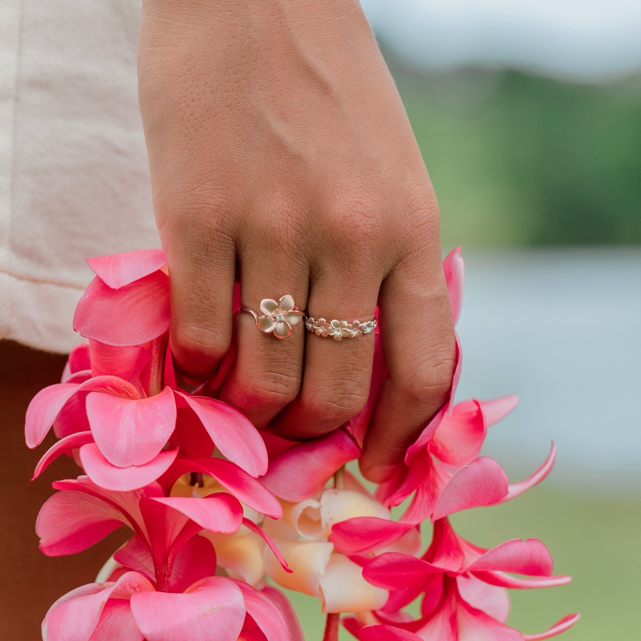 Hand holding pink plumeria lei with Plumeria Rings in Tri Color Gold with Diamonds