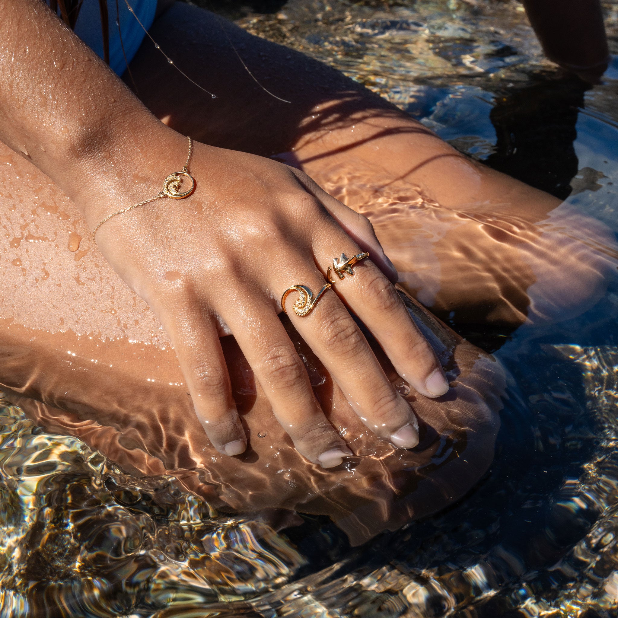 Person sitting in the ocean wearing Nalu Ring and bracelet in Gold with Diamonds