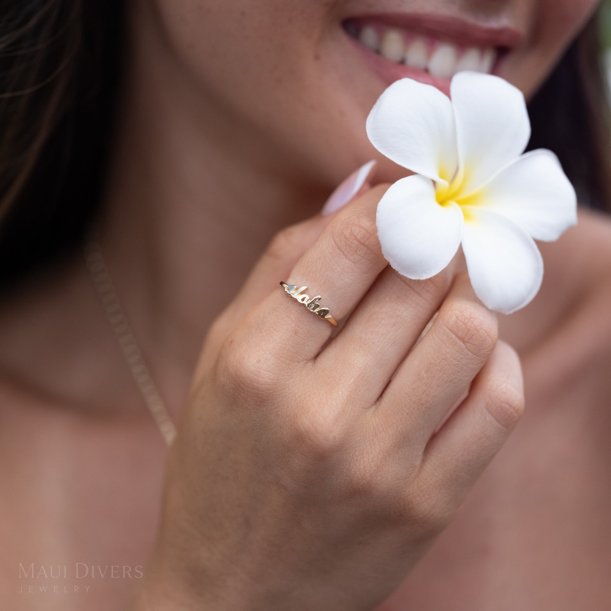 Smiling person holding a plumeria and wearing a 14k yellow gold ʻalohaʻ script ring in 14k yellow gold
