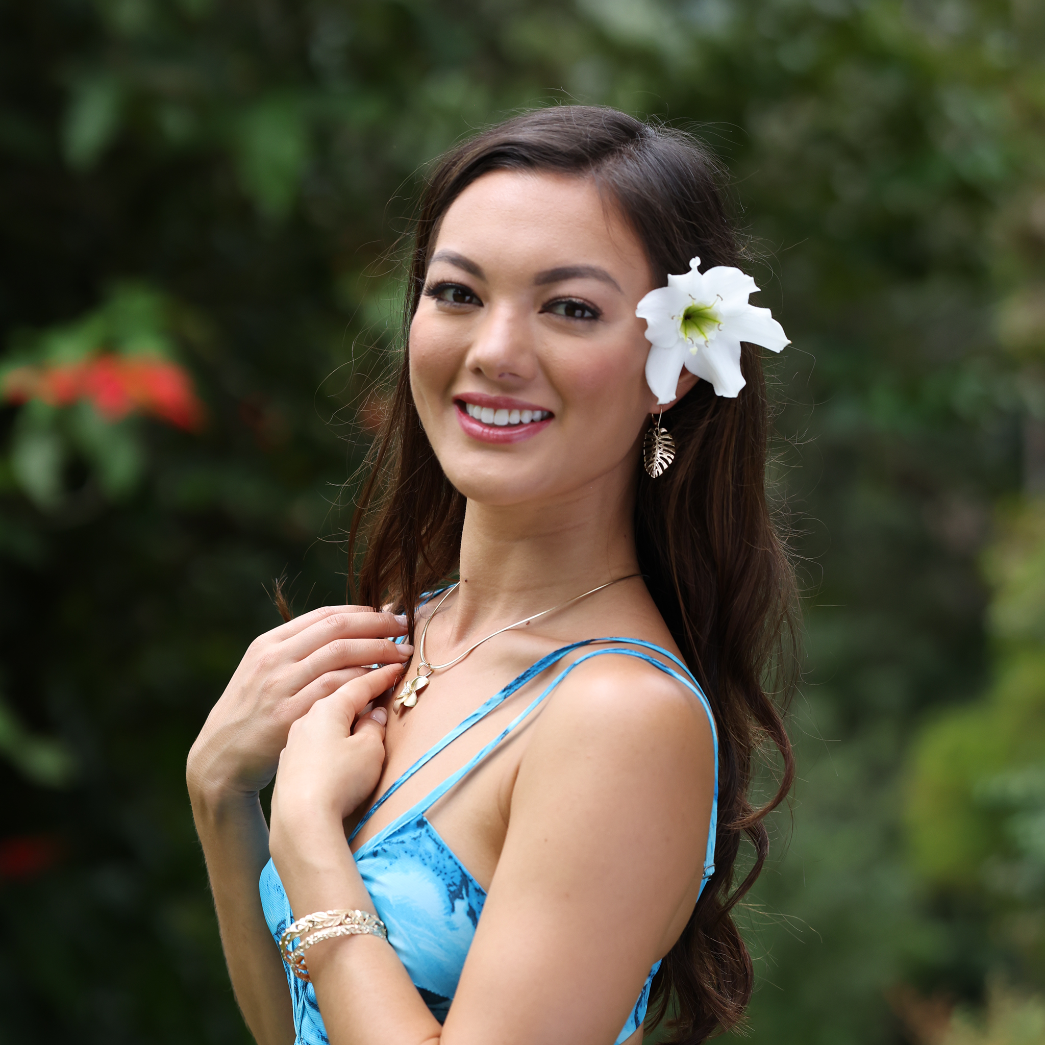 A woman wearing Monstera Earrings in Gold and a Plumeria Pendant out in a garden