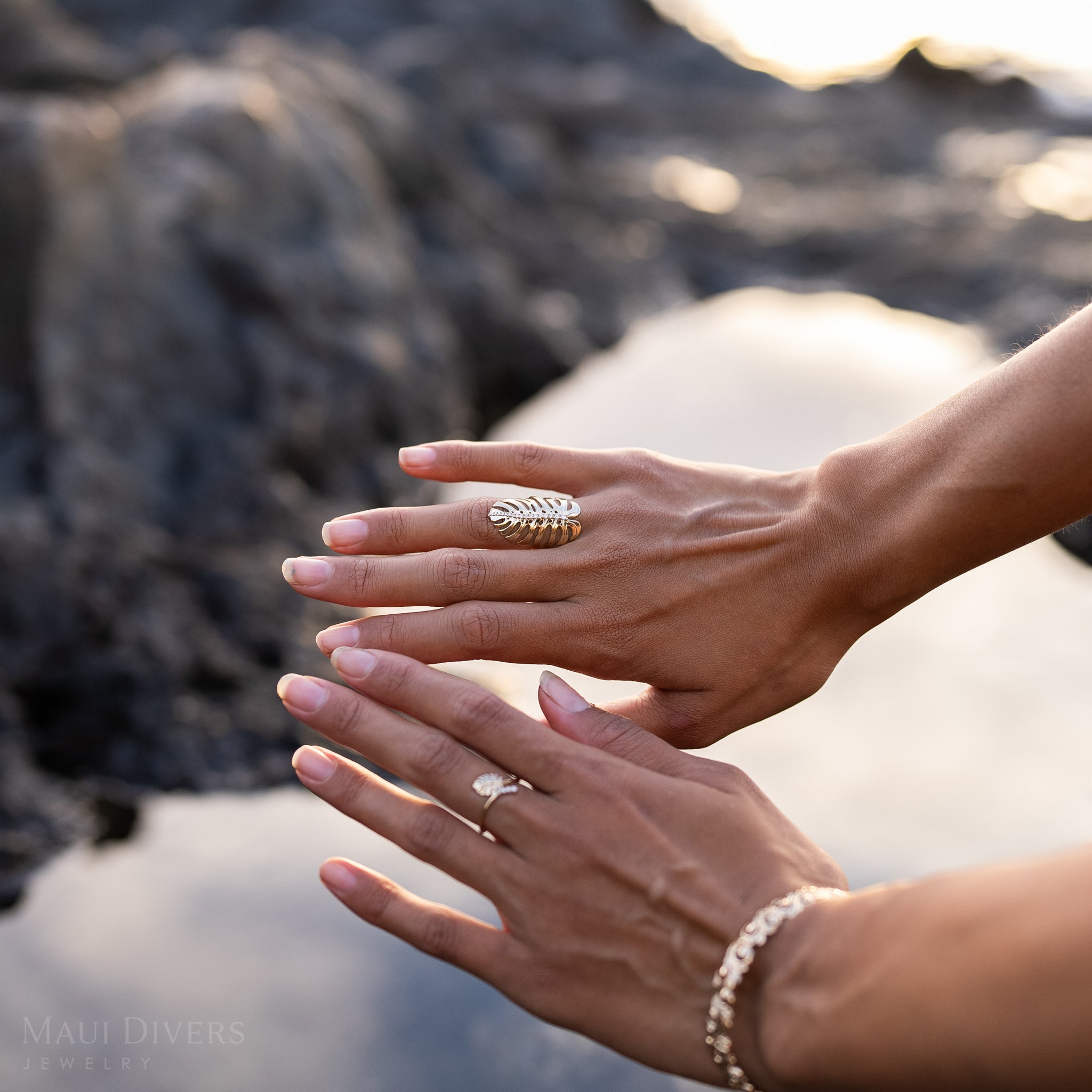 32mm Monstera Ring in Gold with Diamonds on hands over a blurred rocky ocean background