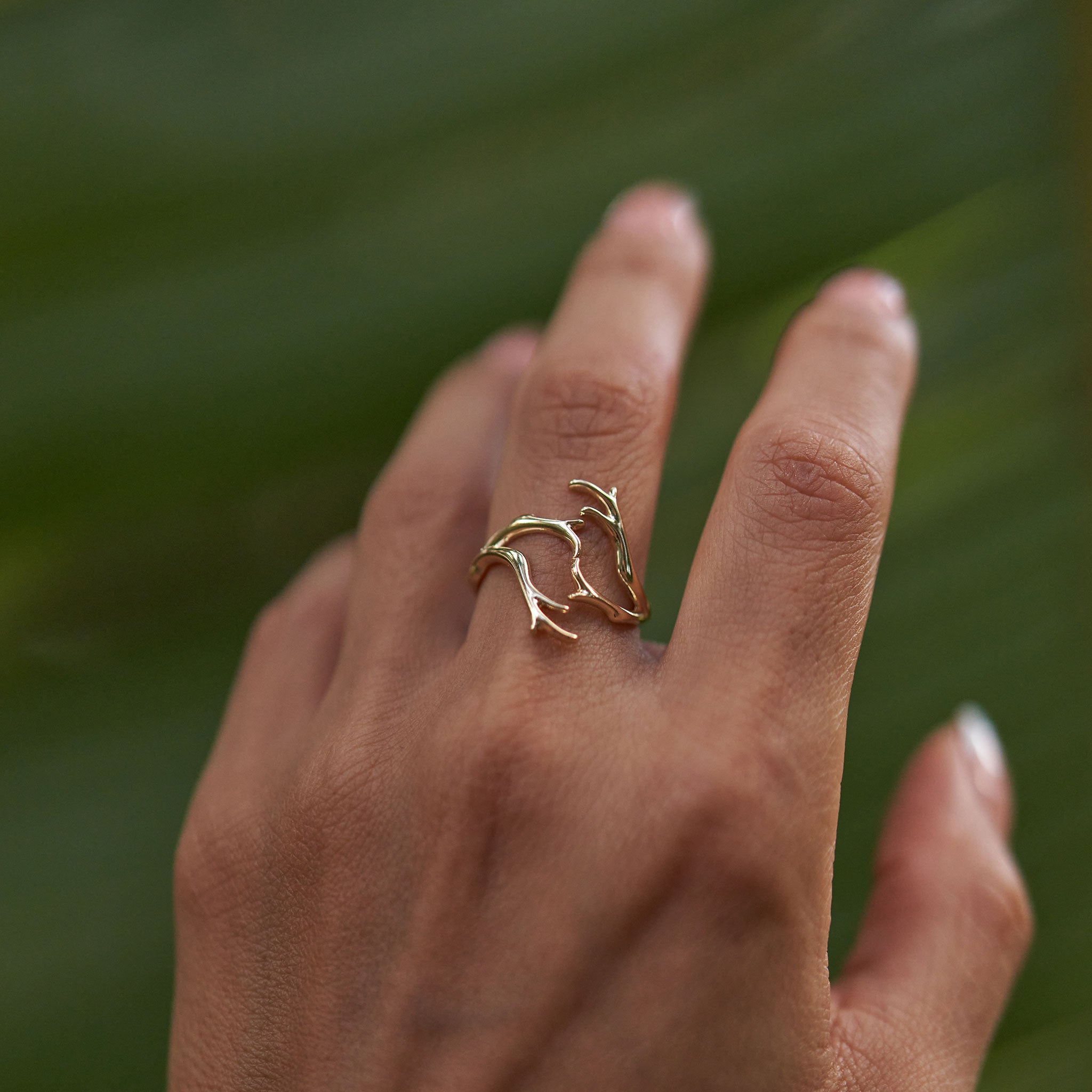 Close up of a Heritage Coral Branch Ring in Gold against a blurred green background