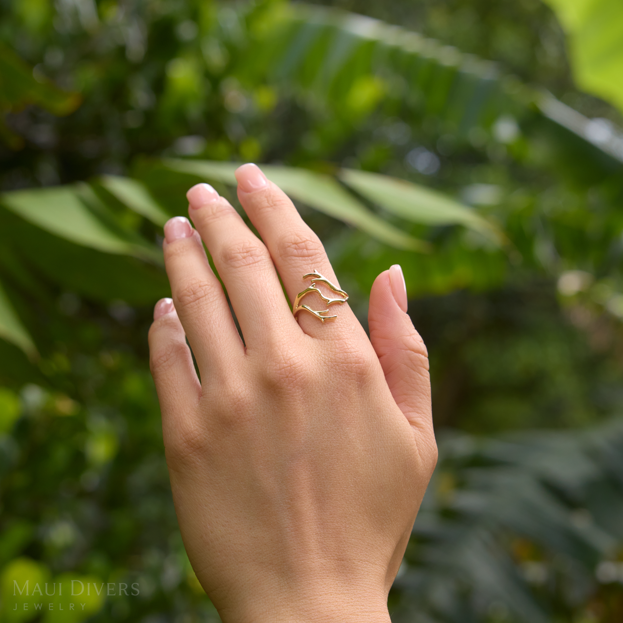 Heritage Coral Branch Ring in Gold on a hand with a blurred green leaf background