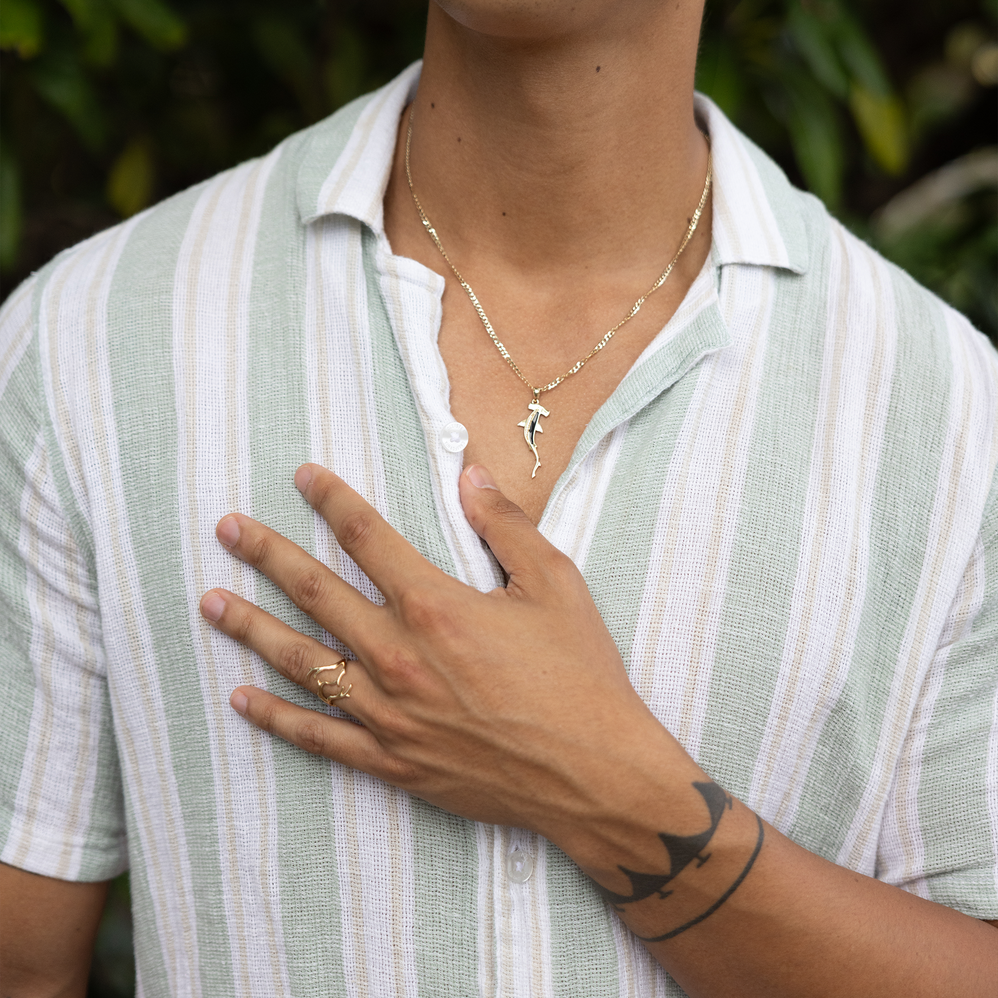 Heritage Coral Branch Ring in Gold and Shark Pendant on a man's chest wit blurred green background