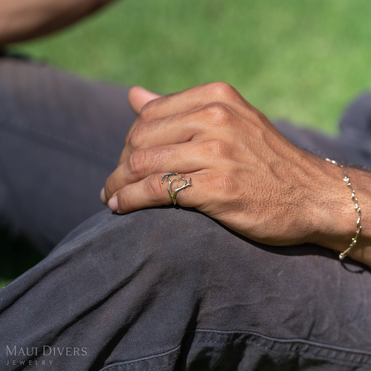 Close-up shot of a man's hand wearing a Heritage Collection coral branch-inspired gold ring as it rests on his black pants