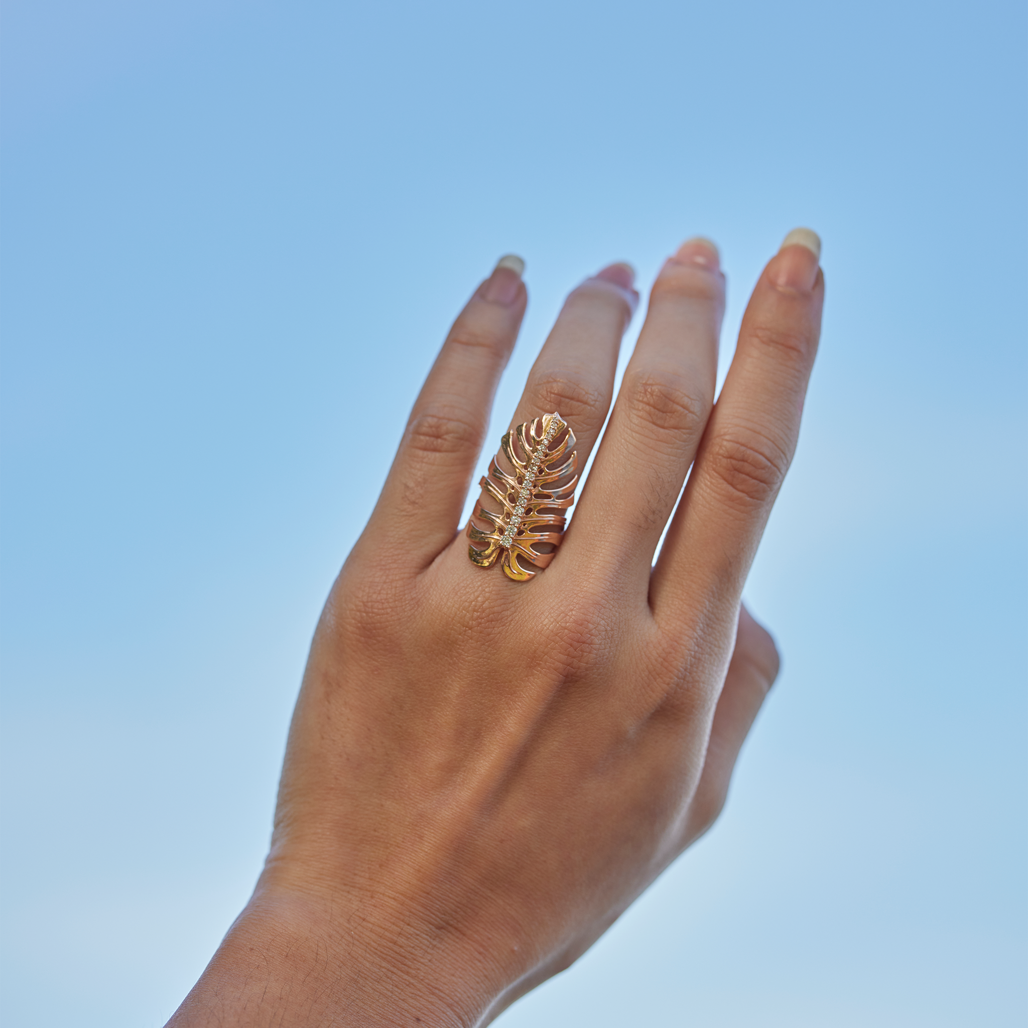 32mm Monstera Ring in Rose Gold with Diamonds on a hand held up against a blue sky