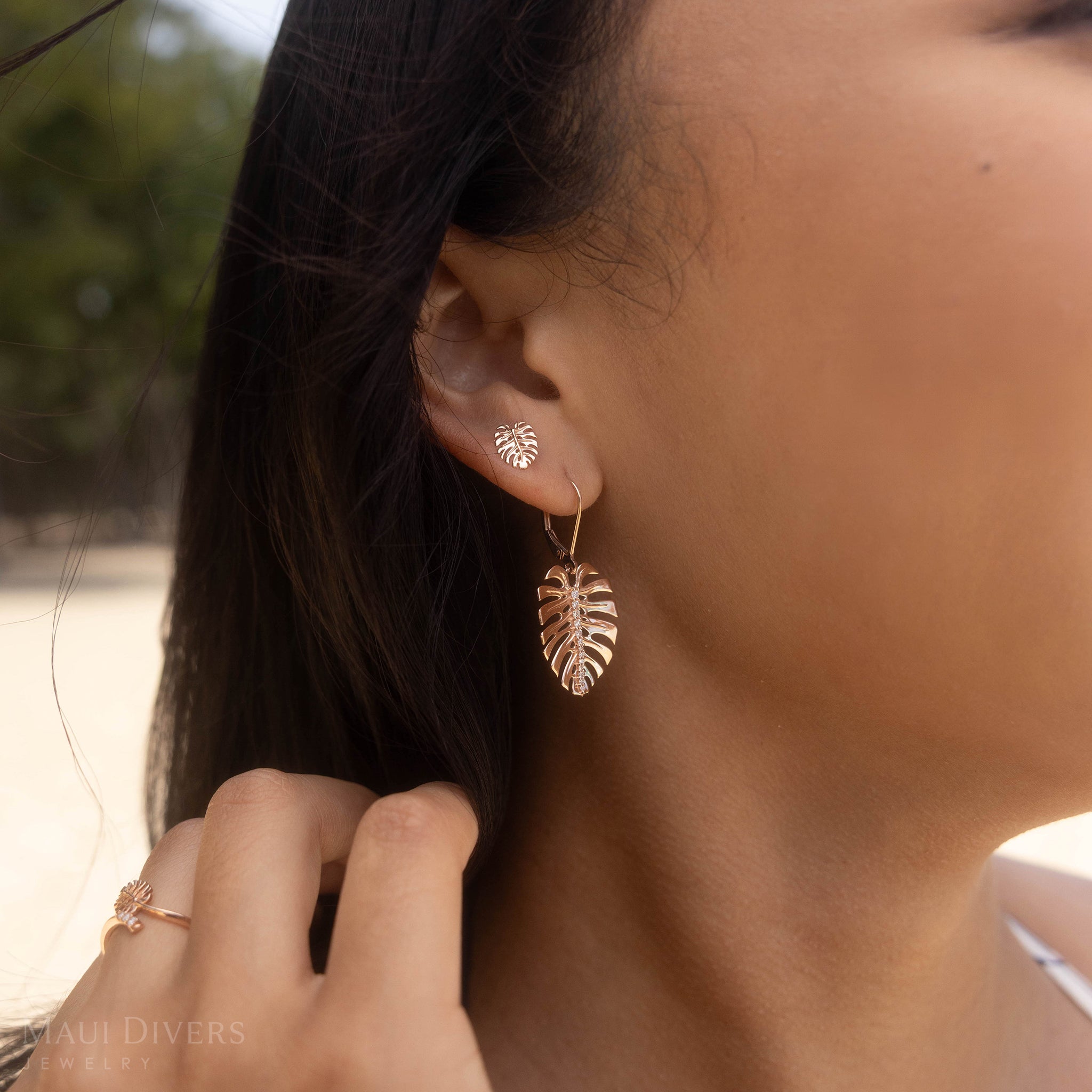 Close-up of a person wearing Two Monstera Earrings in Rose Gold with Diamonds with a blurred background