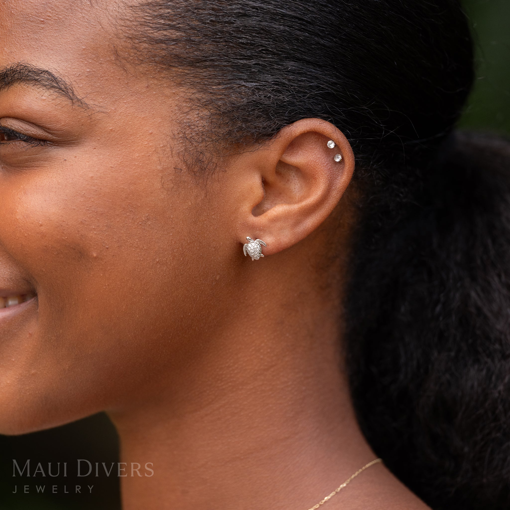 Close-up of a smiling woman wearing a Honu Earring in 14k White Gold with Diamonds against a blurred background