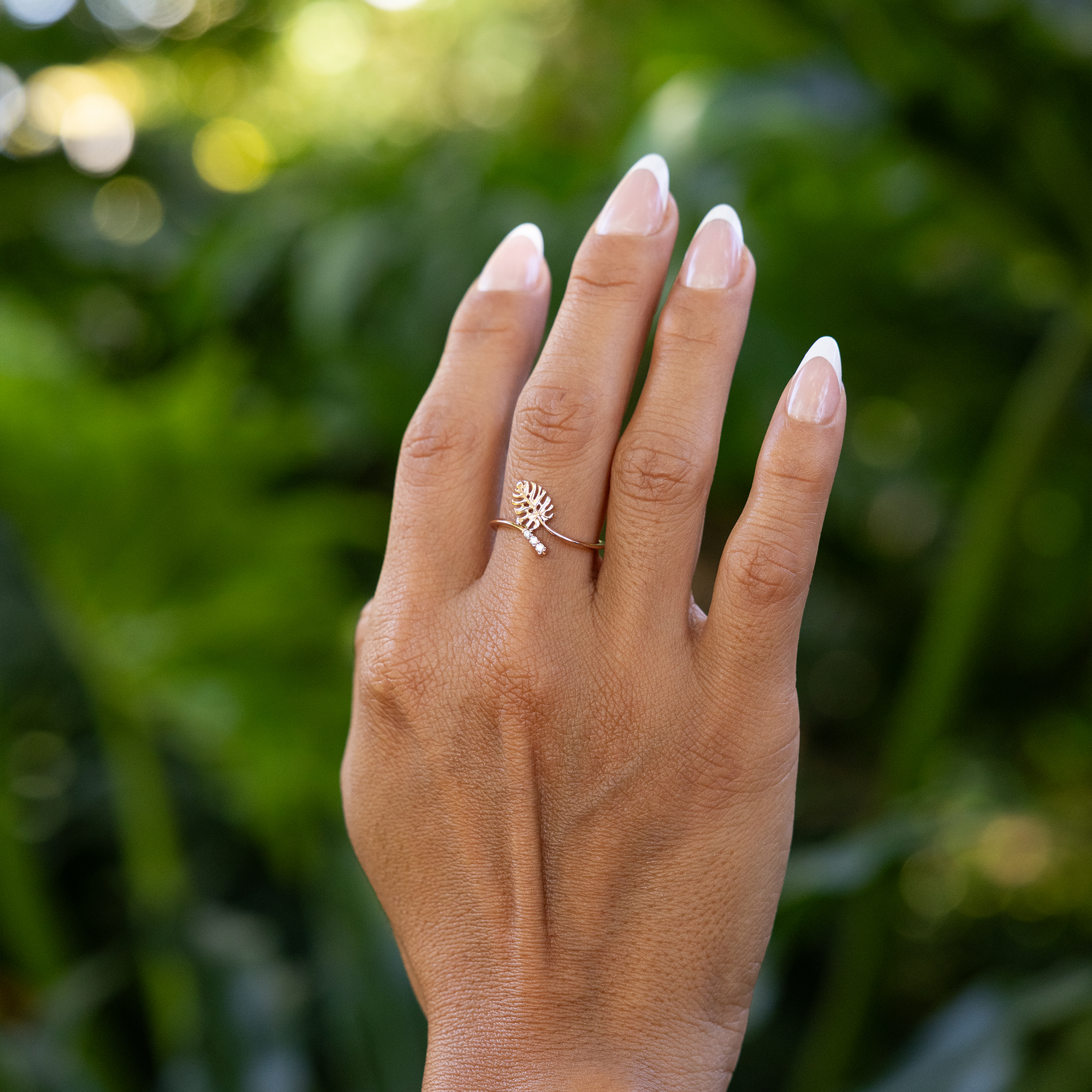 Close up of 9mm Monstera Ring in Rose Gold with Diamonds on a hand over blurred leaves
