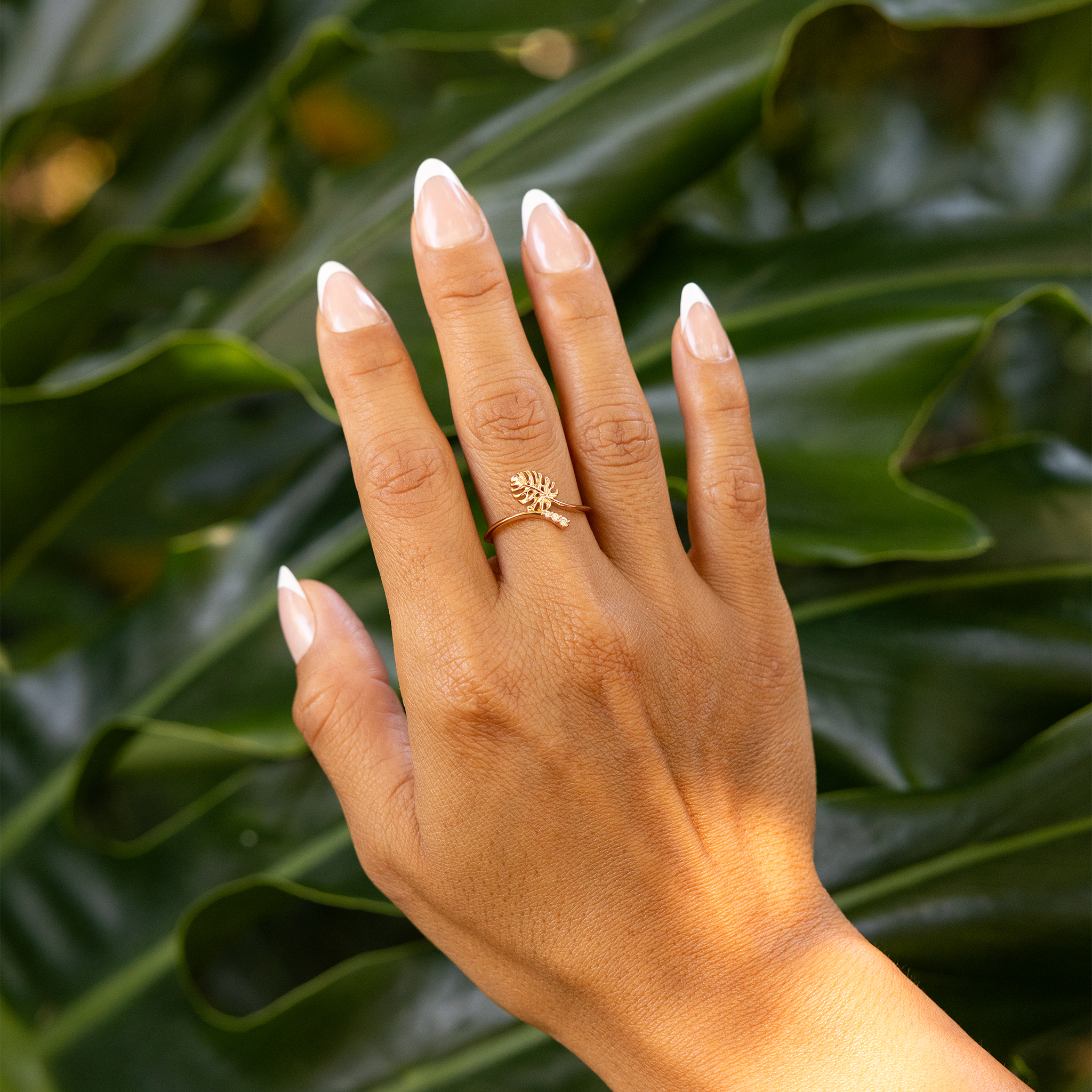 Close up of 9mm Monstera Ring in Rose Gold with Diamonds on a hand over blurred dark leaves