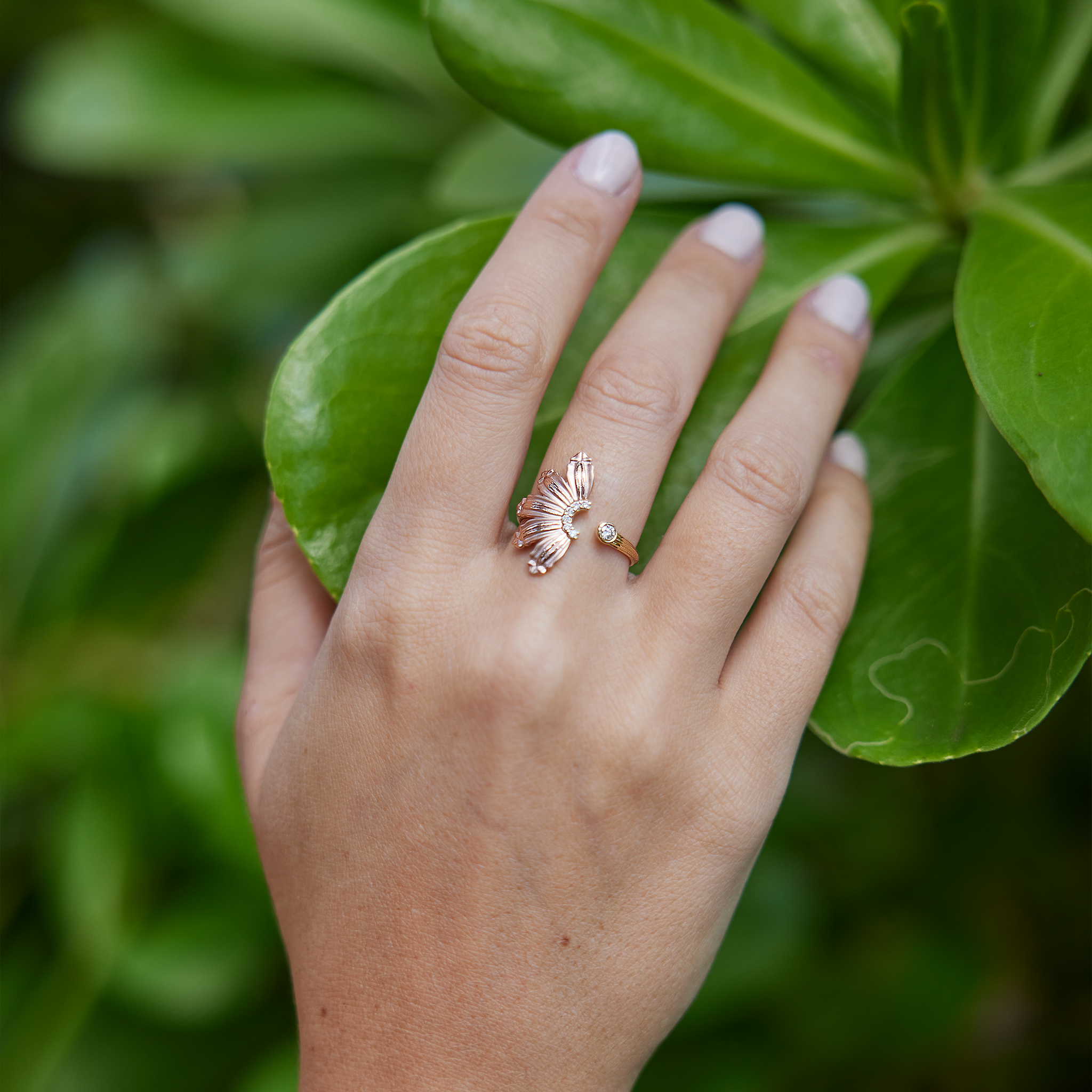 Woman's hand over a leaf wearing a Mountain Naupaka Ring in Two Tone Gold with Diamonds