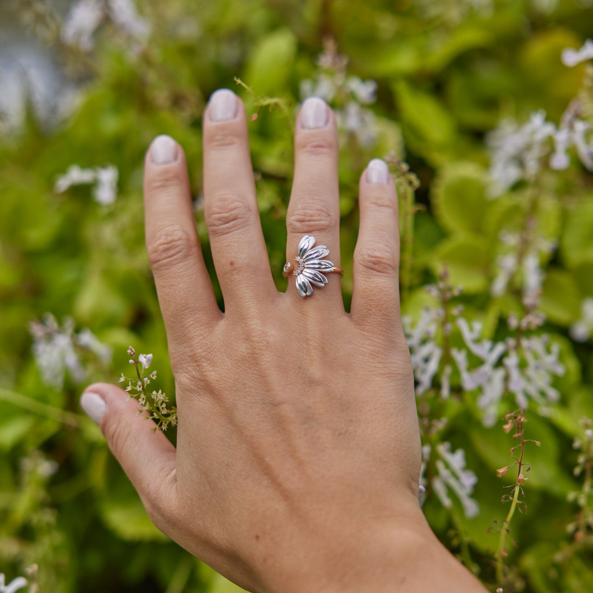 Womanʻs hand wearing Beach Naupaka Ring in Two Tone Gold with Diamonds with foliage background