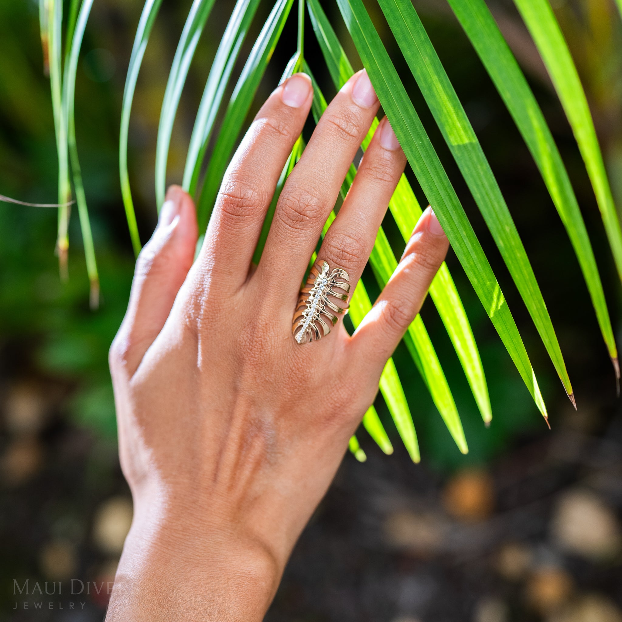 32mm Monstera Ring in Gold with Diamonds on a hand touching palm leaves