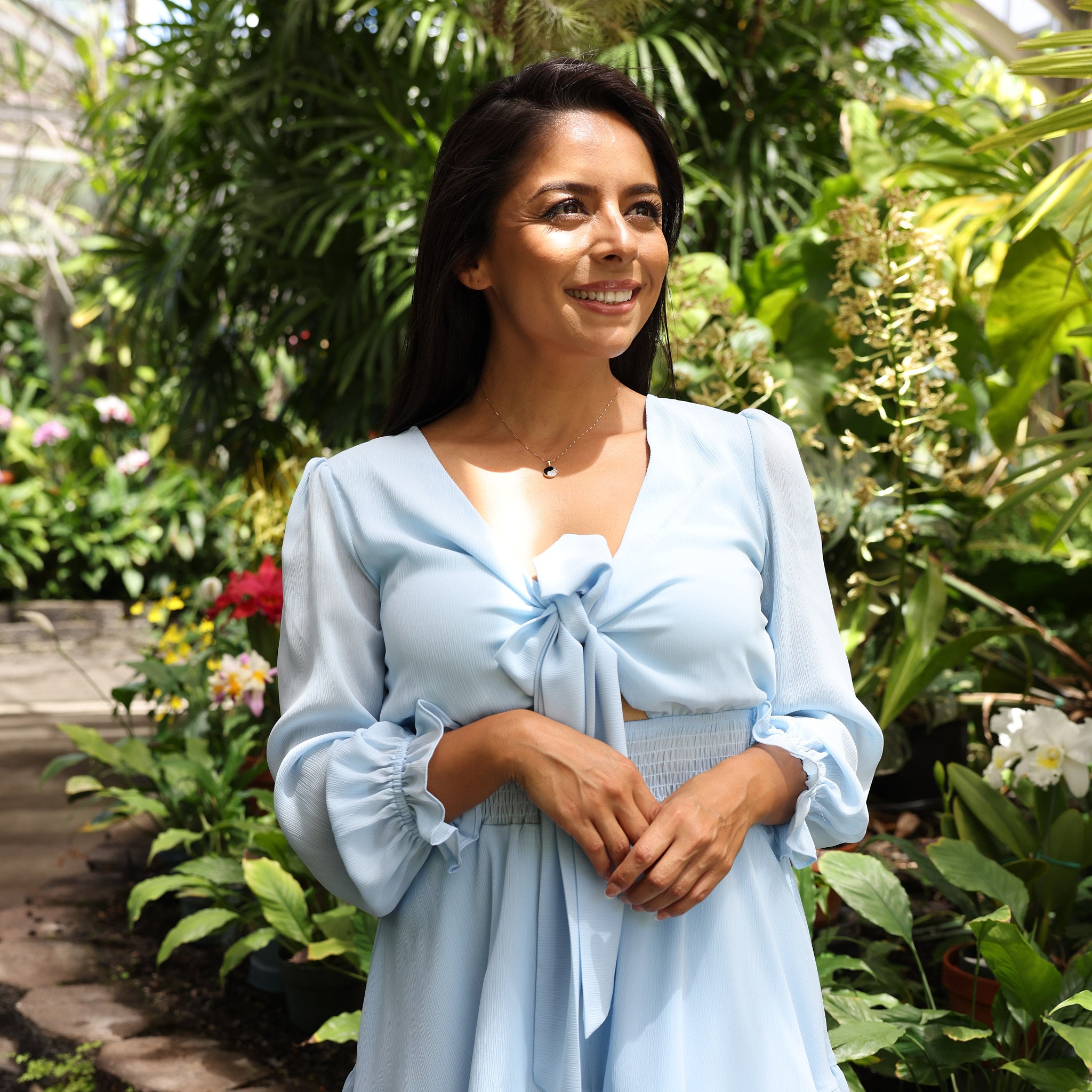 woman in blue dress wearing Yin Yang Black Coral Pendant in Gold with Diamonds - 12mm through Hawaii botanical garden