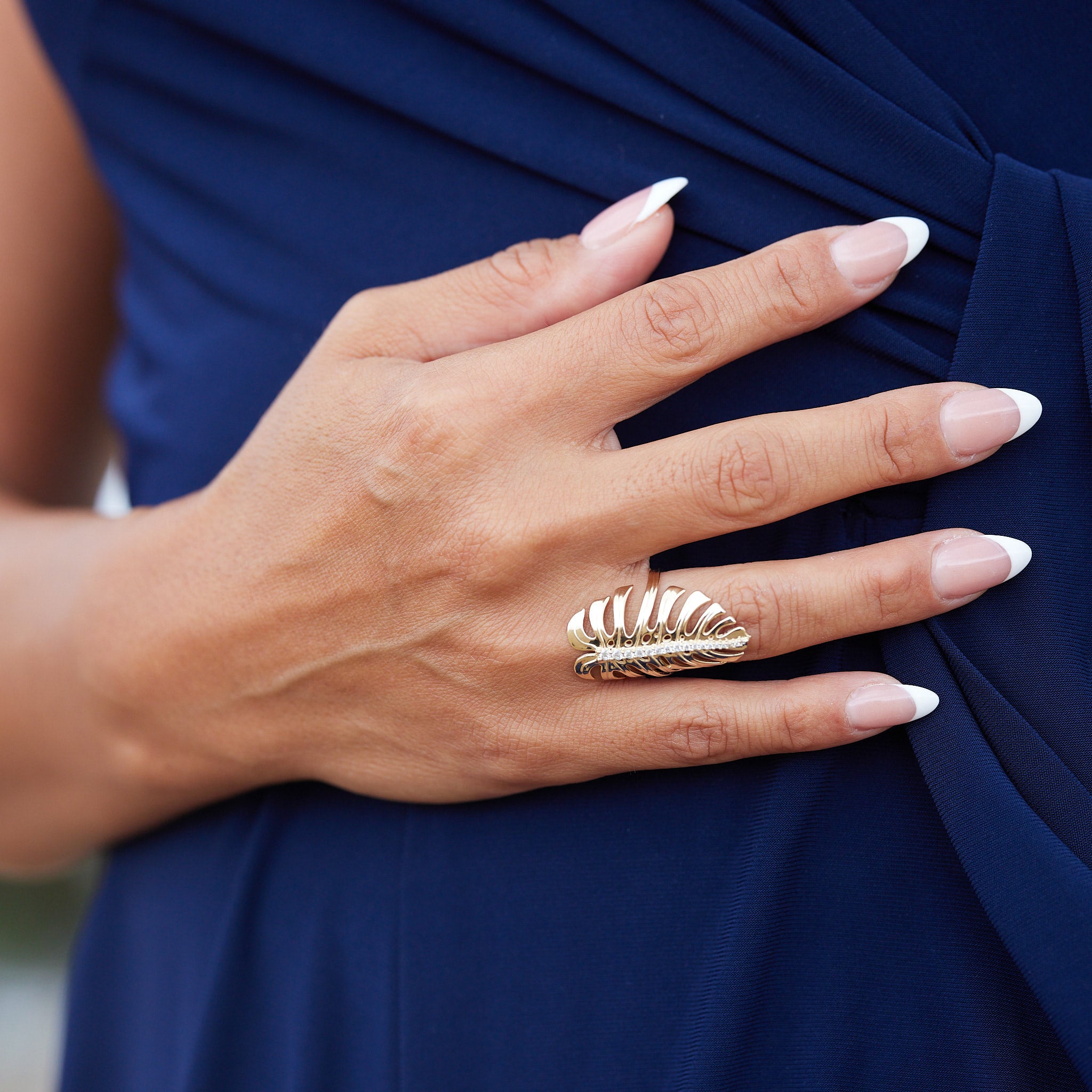 A woman's hand with a 32mm Monstera Ring in Gold with Diamonds resting against a blue dress