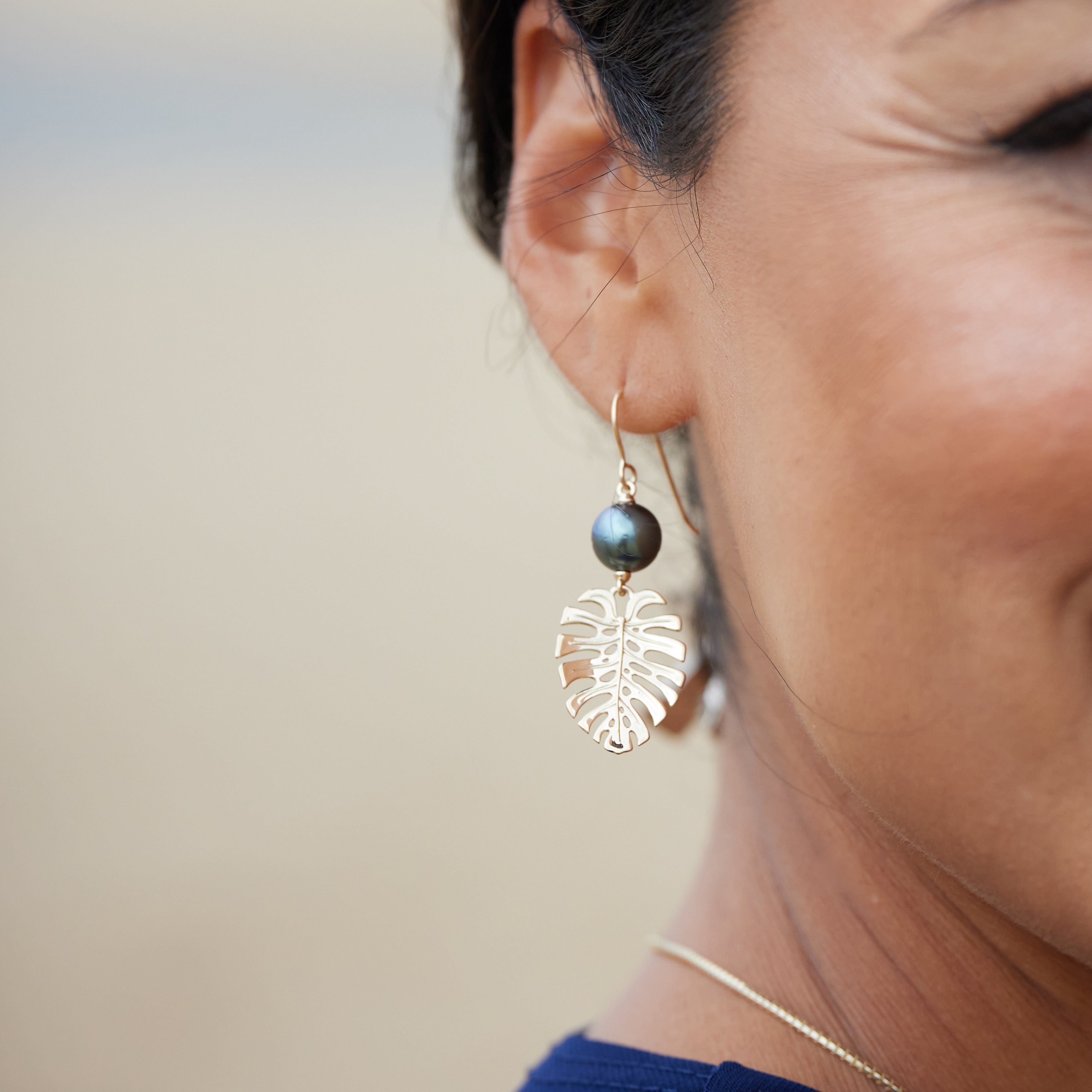 A woman's ear with 23mm Monstera Tahitian Black Pearl Earrings in Gold