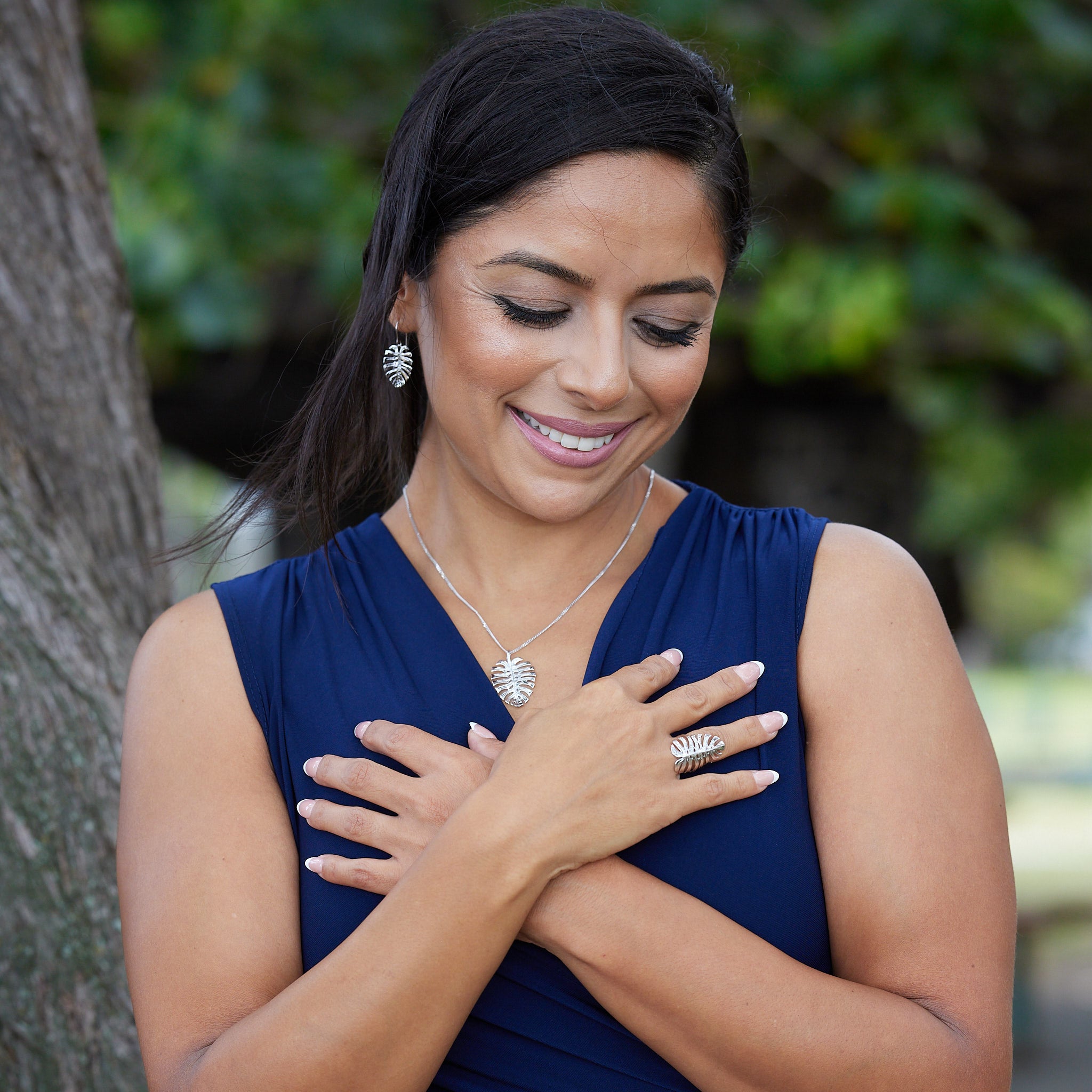 A woman wearing Monstera Earrings, Pendant and Ring in White Gold with a blurred park background