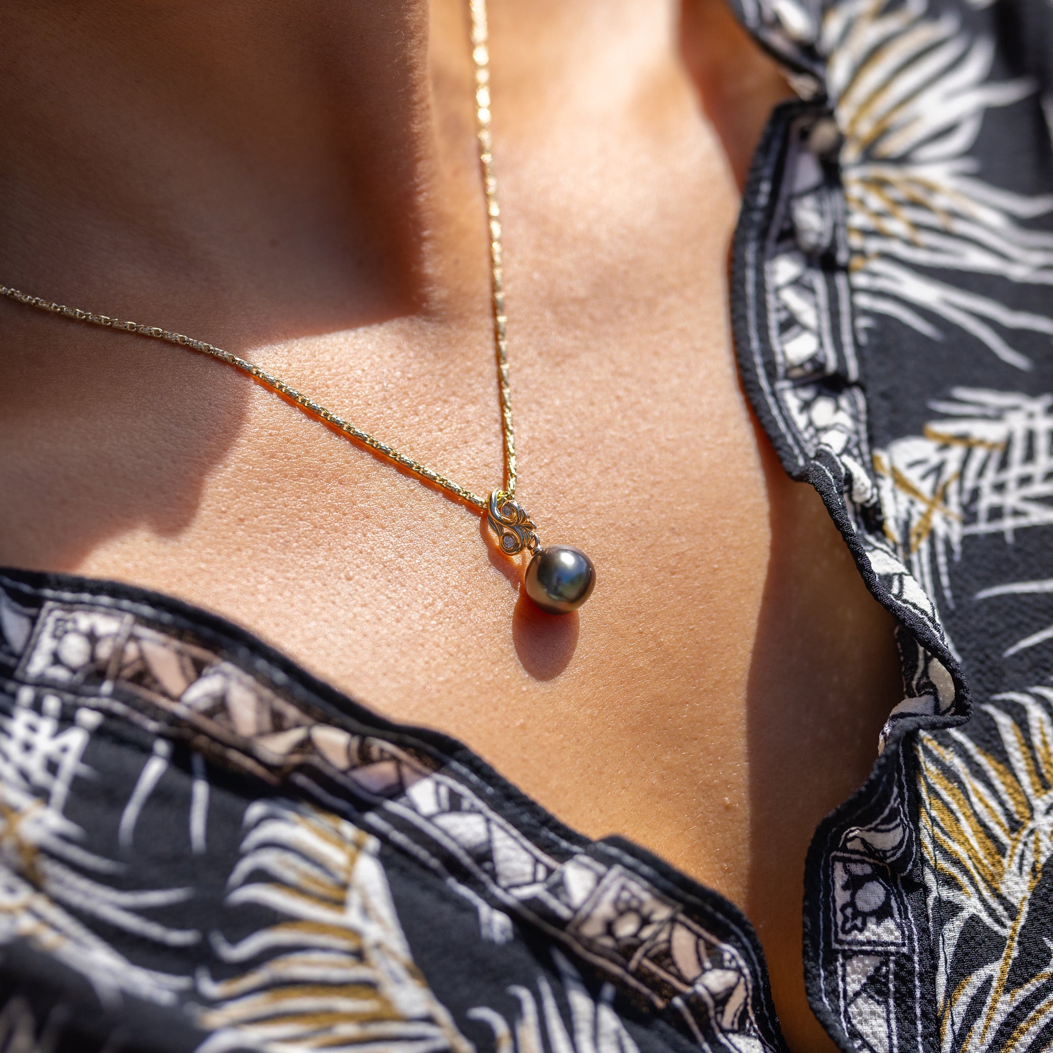 Close up of a person wearing the Living Heirloom Tahitian black pearl pendant in 14k yellow gold with diamond accents on a 14k yellow gold chain