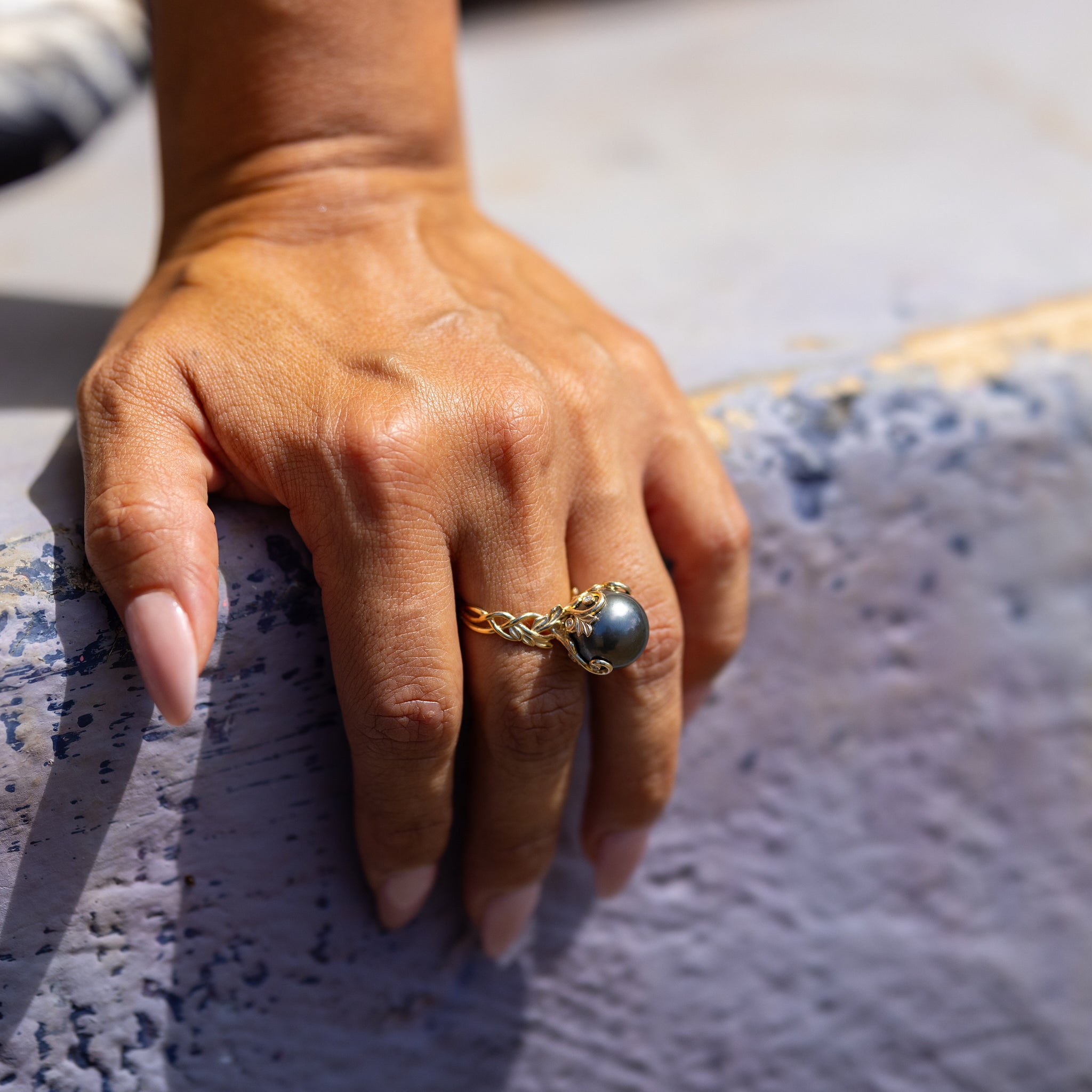 Tahitian Black Pearl Ring with Ornate Design in Gold on Finger with cement background - Maui DIvers Jewelry
