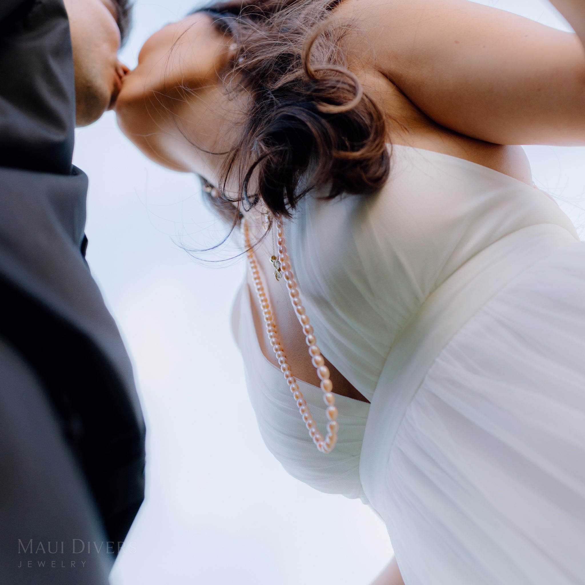 Woman wearing a white dress with a long peach pearl necklace and plumeria pendant