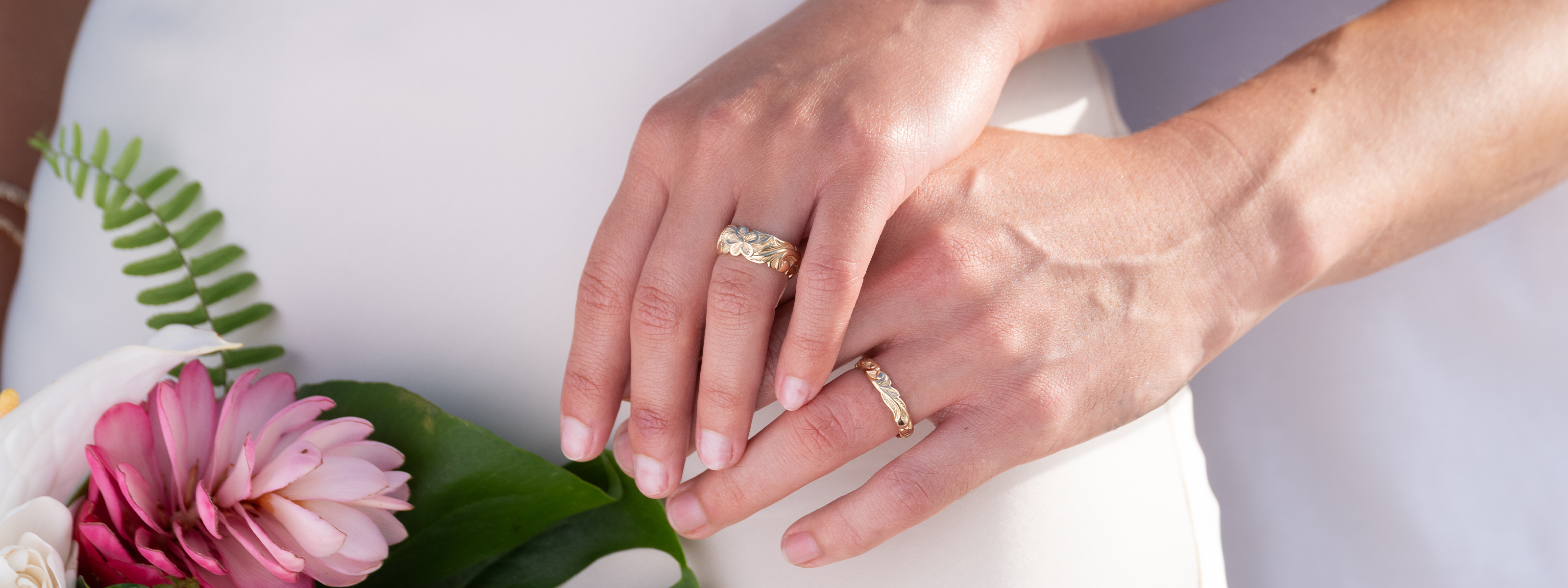 Two hands with Hawaiian Heirloom wedding rings holding a bouquet of flowers.