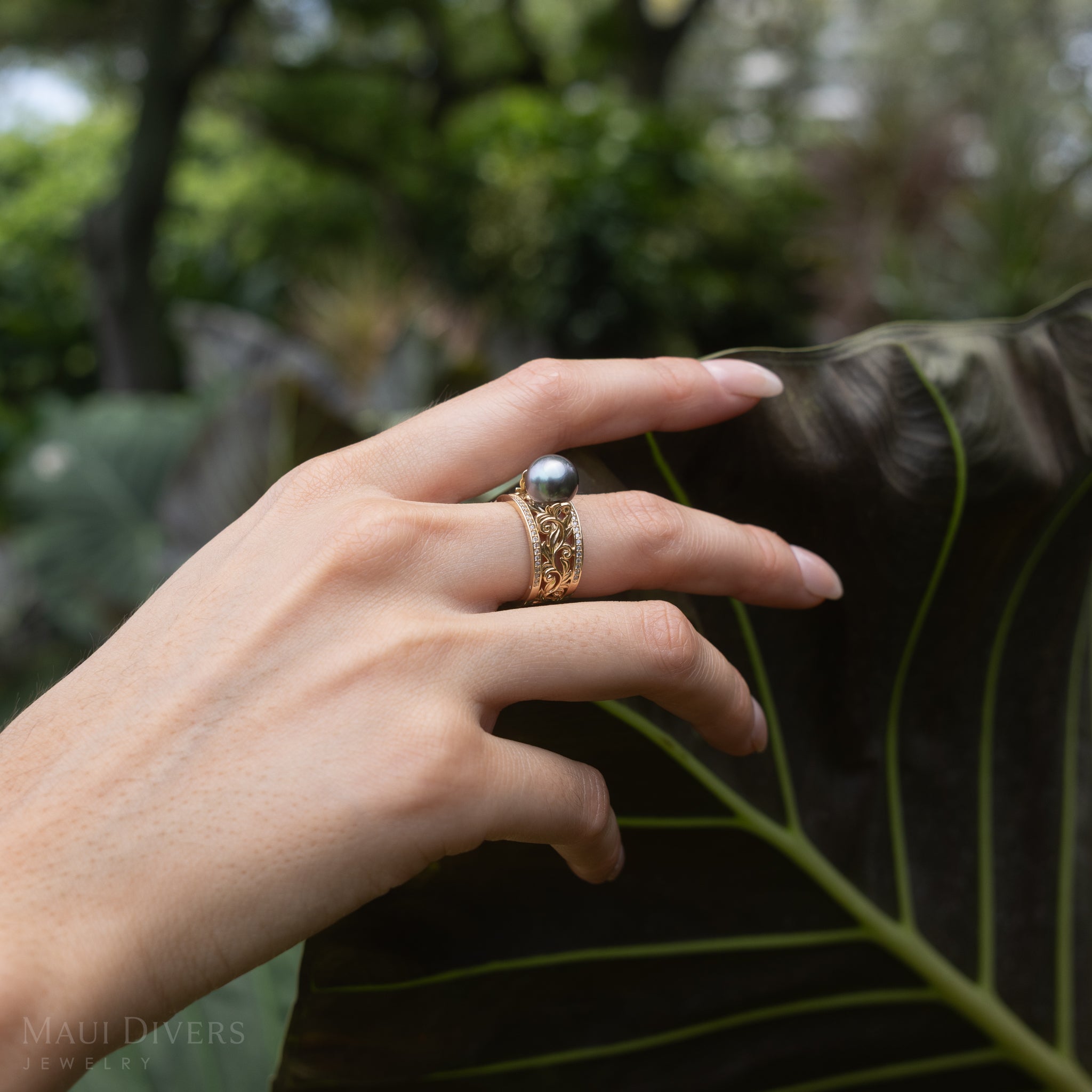 Hand wearing a Living Heirloom Tahitian Black Pearl Ring in Gold with Diamonds on a large green leaf