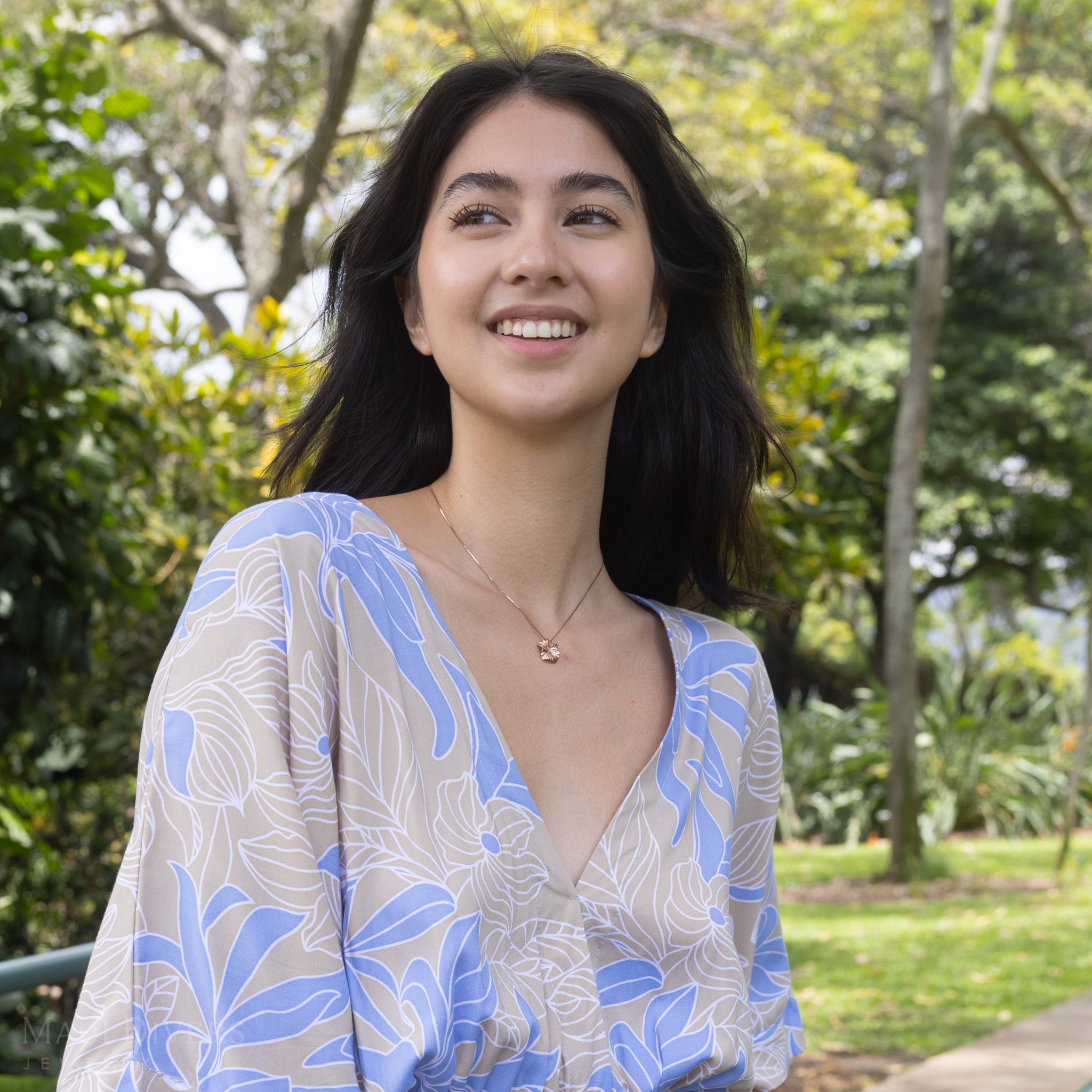 Woman wearing a rose gold diamond hibiscus pendant with a blurry forest background